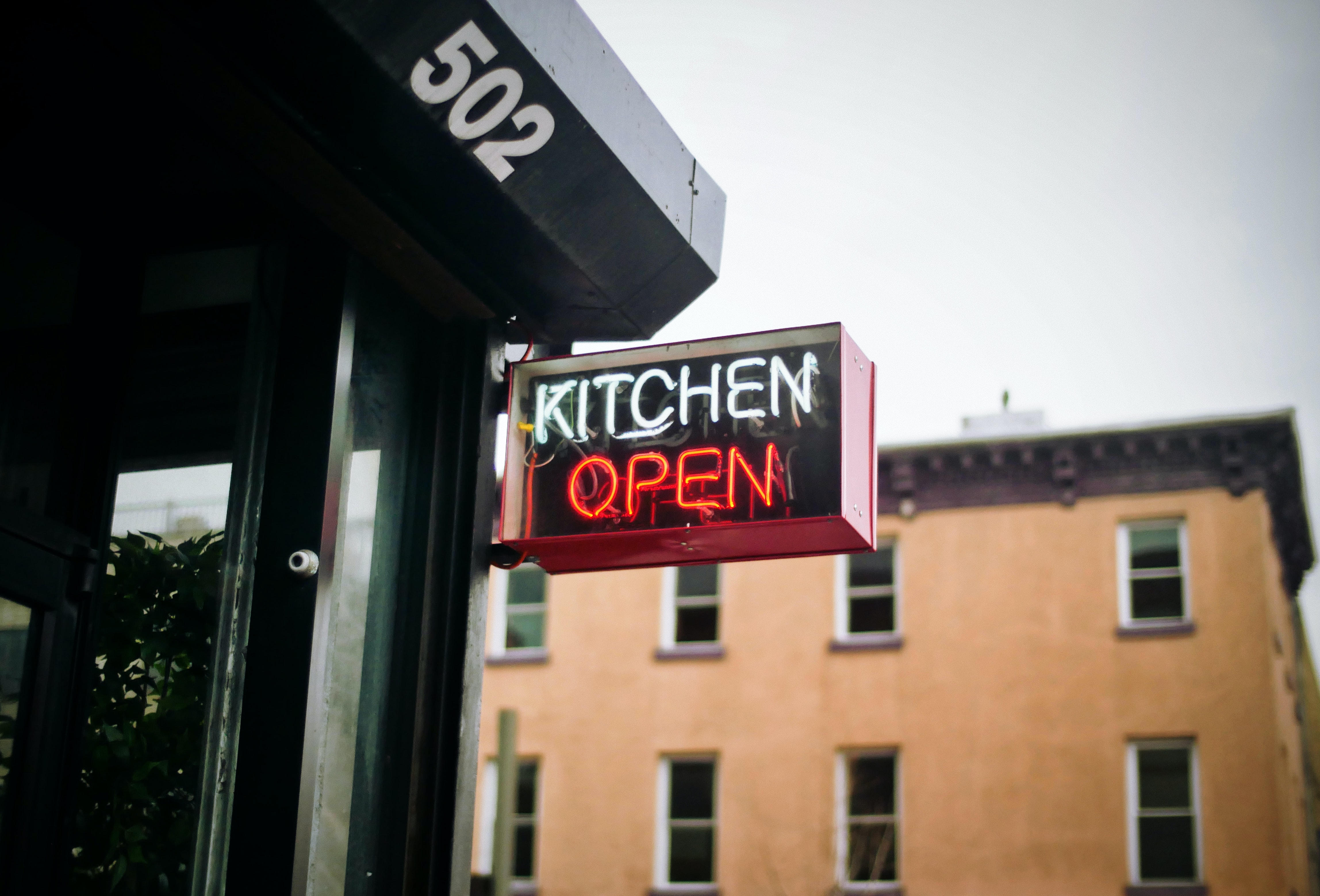 A lit up sign saying "Kitchen Open" outside of a restaurant.