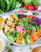 A beautiful leafy salad on a white table cloth surrounded by vegetables. 