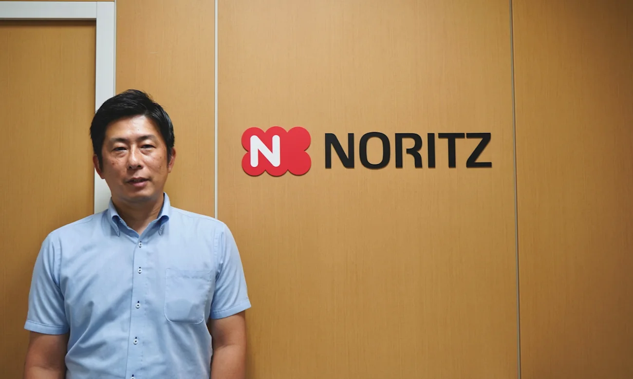 NORITZのロゴが掲げられた壁の前に立つ取材対象者