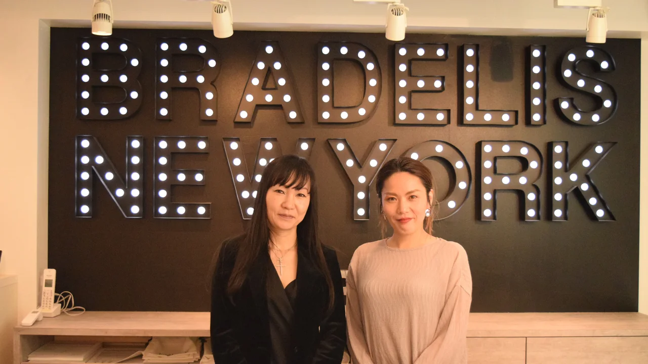 BRADELIS NEW YORKのロゴサインを背に立つ取材対象者2名