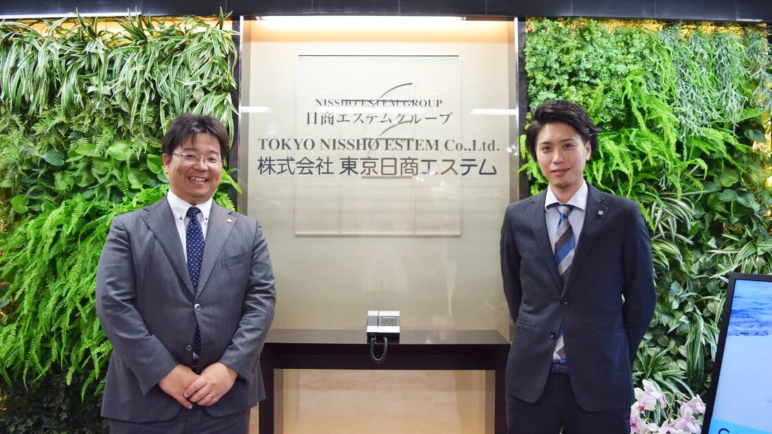 株式会社東京日商エステムの社名プレート前に立つ取材対象者2名
