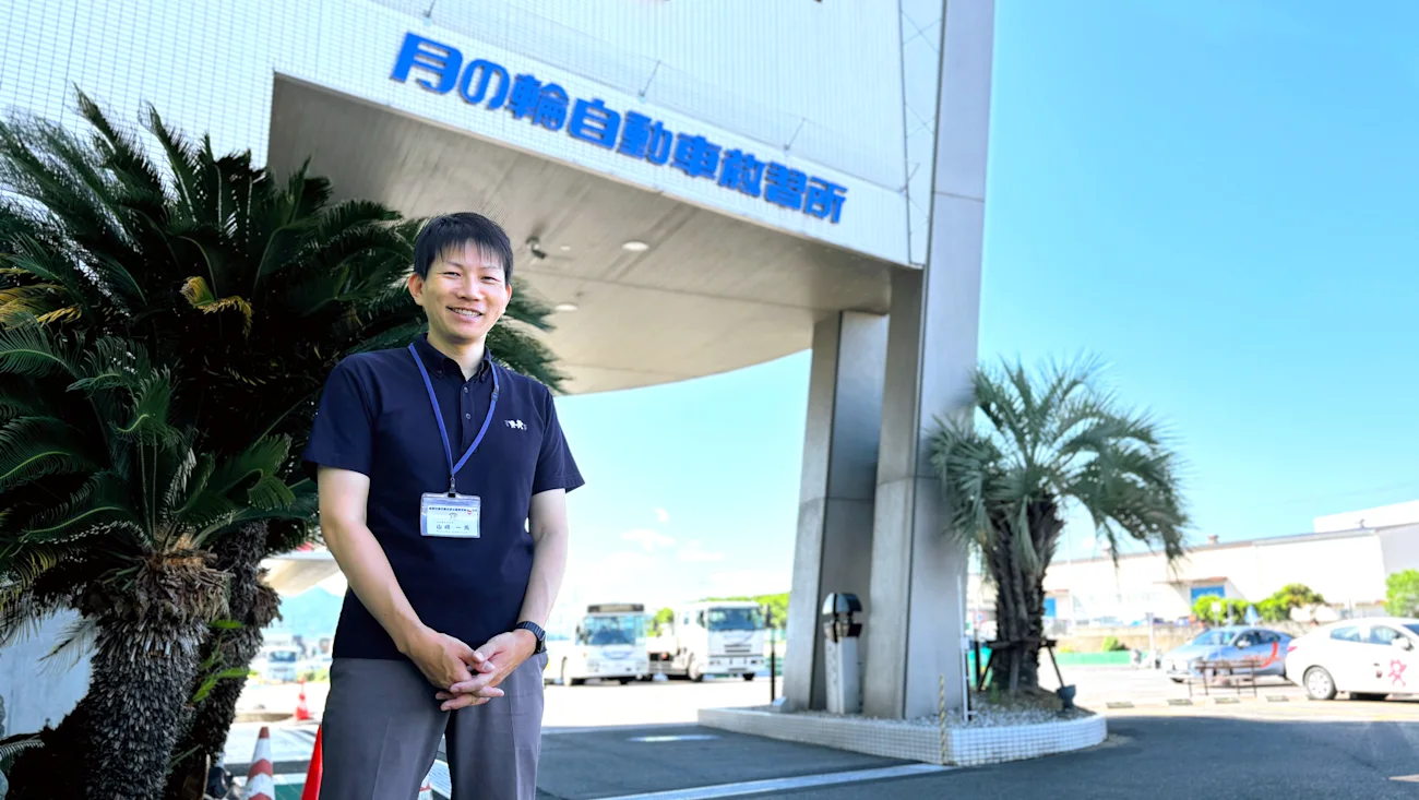 月の輪自動車教習所の正門前に立つ担当者