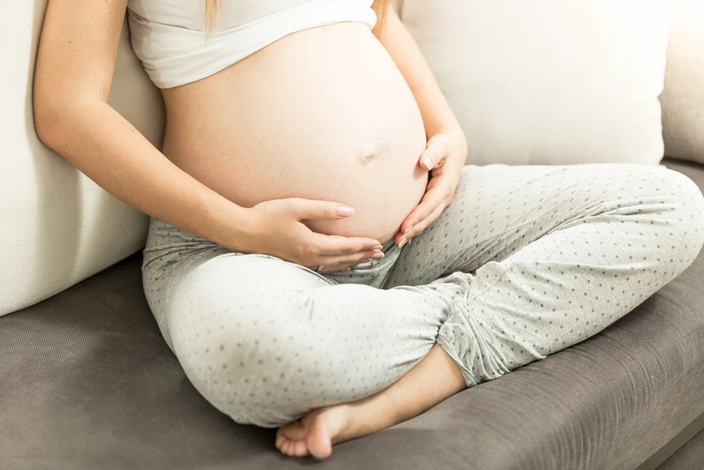 young pregnant woman sitting on couch and holding tummy