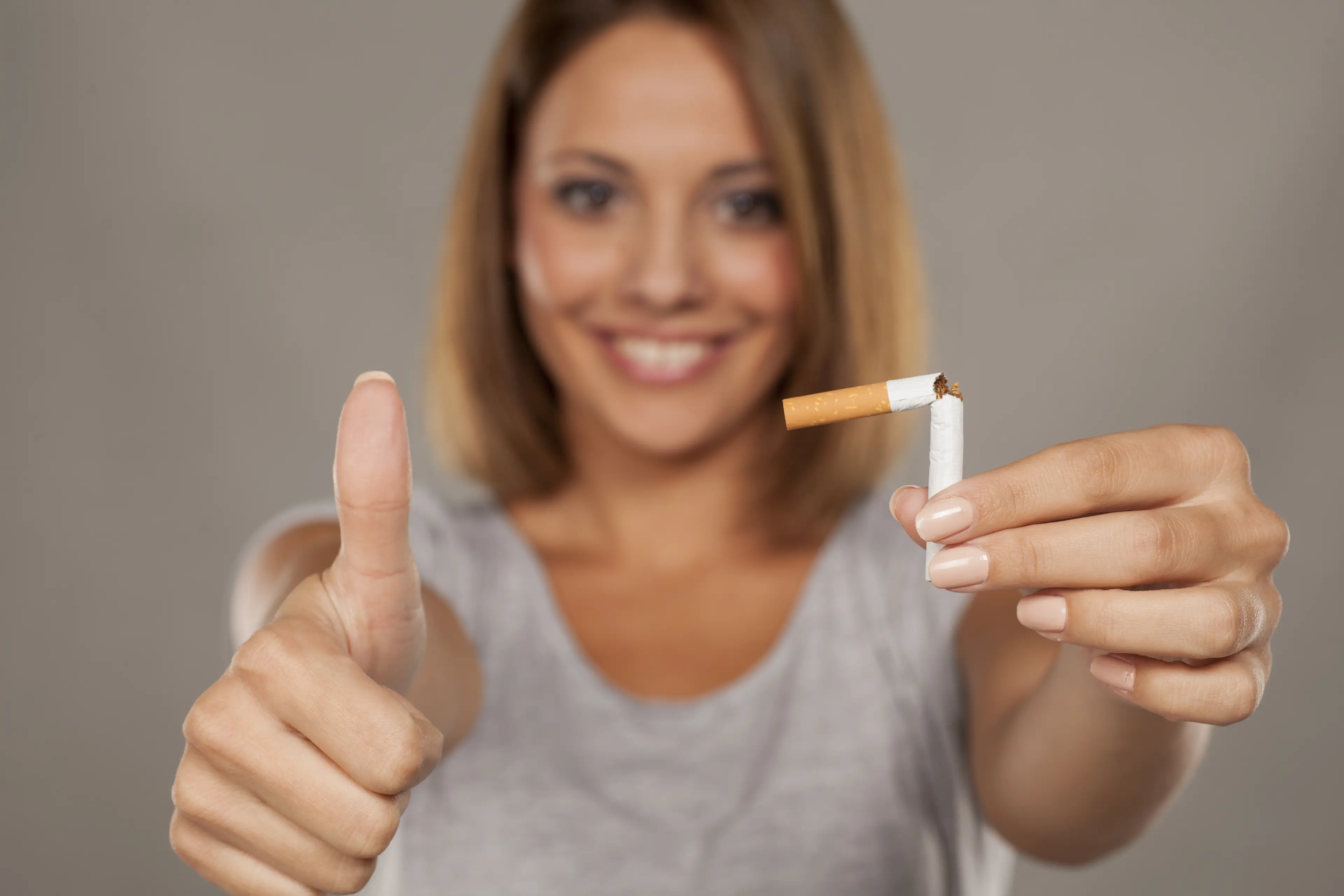 young happy woman holding a broken cigarette and showing thumbs up