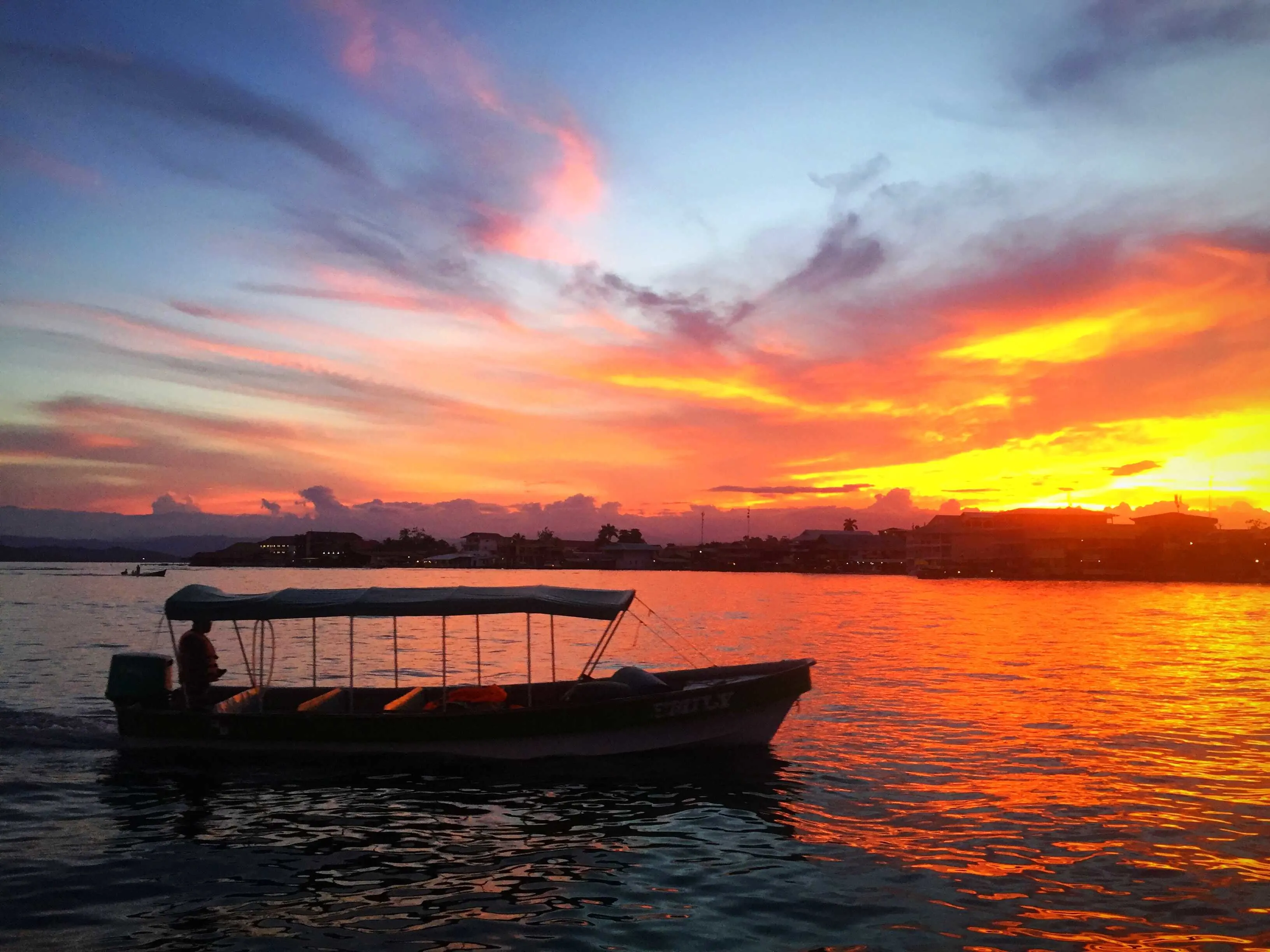 A fiery sunset over Isla Carenero, with a water taxi gliding through the glowing waters. 