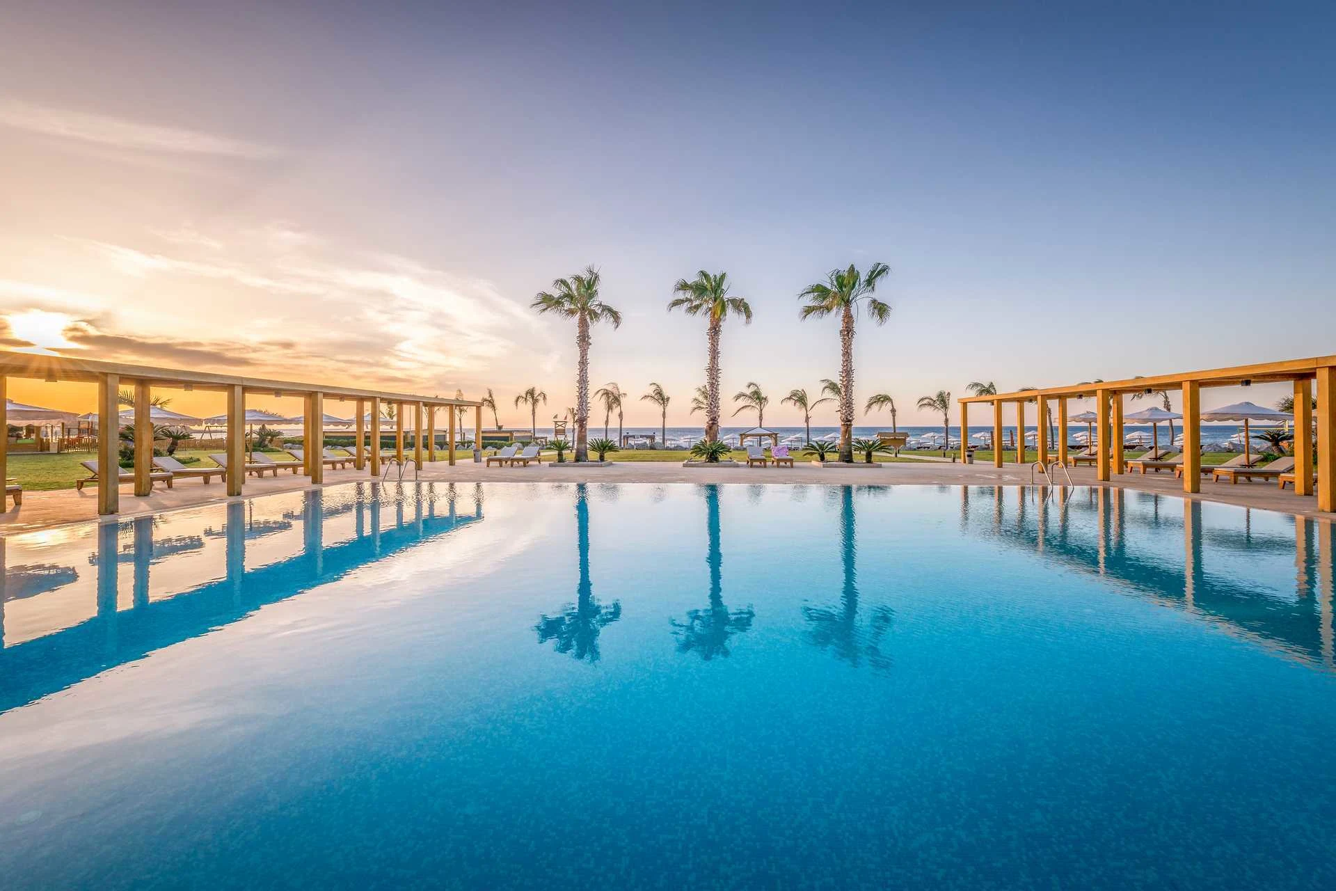 Fra bassengområde på Mitsis Selection Alila Exclusive Resort & Spa med et stort basseng, palmer og et glimt av havet i bakgrunnen.