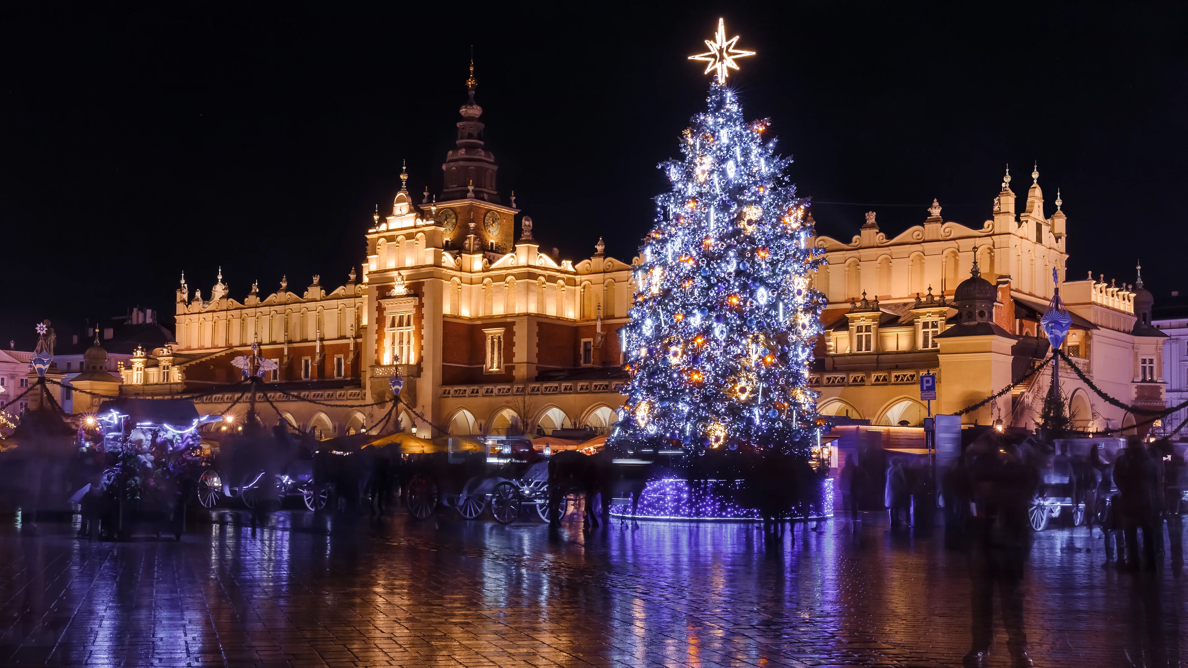 Julgran på julmarknaden i Krakow på Rynek Główny framför den upplysta Tyghallen en vinterkväll