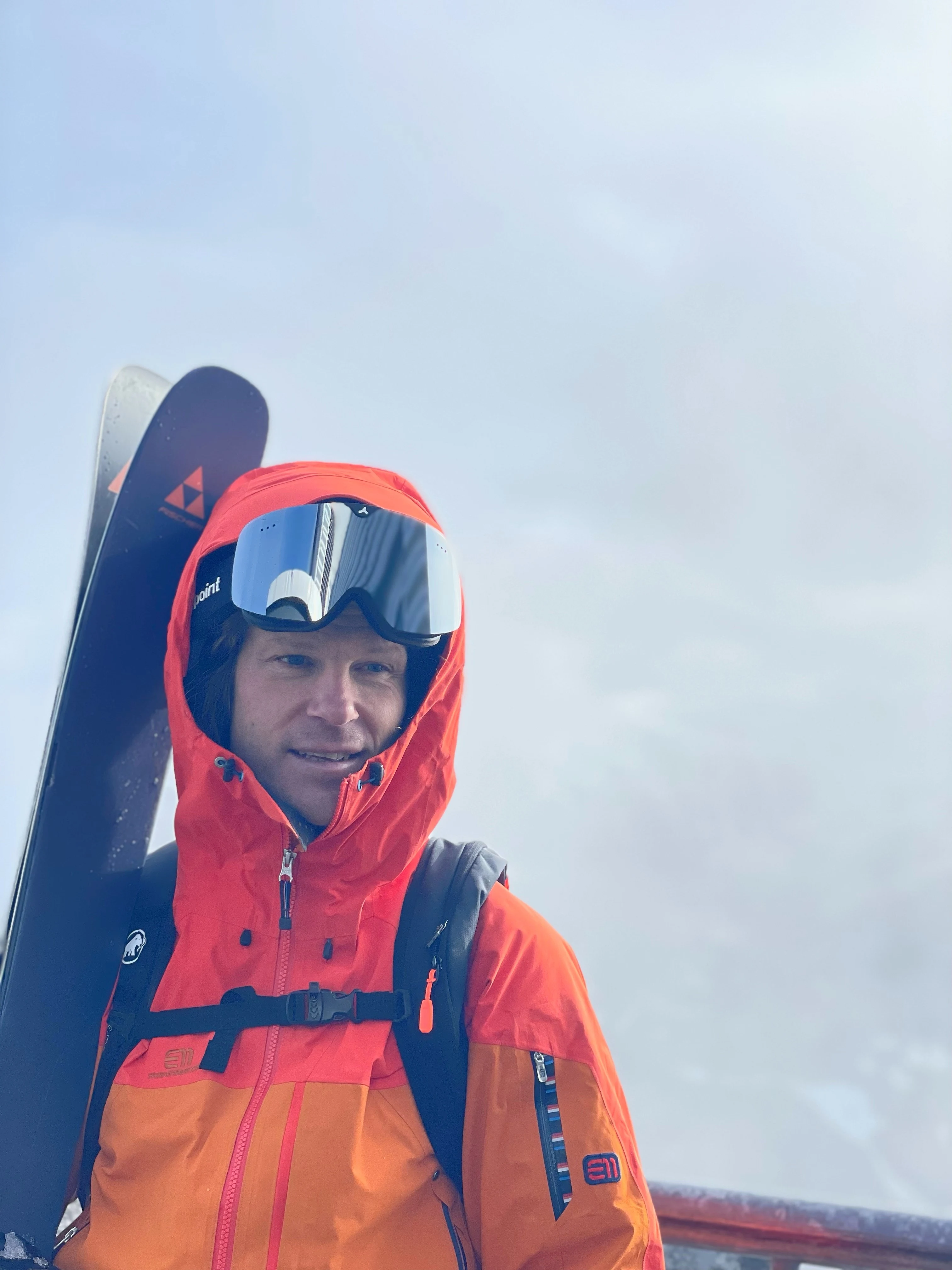 Tobias Granath i röd skidjacka med skidor på axeln i dimmigt bergslandskap