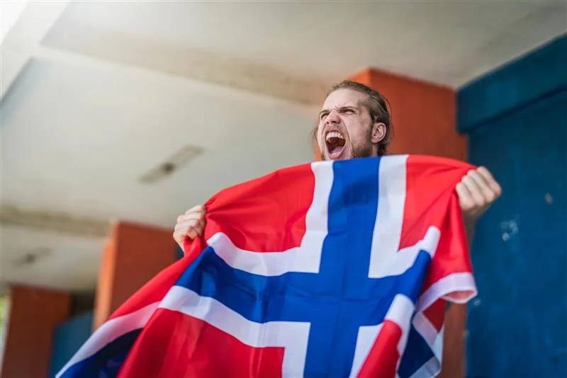 Supporter på fotballkamp som roper og holder et norsk flagg i begge hender.