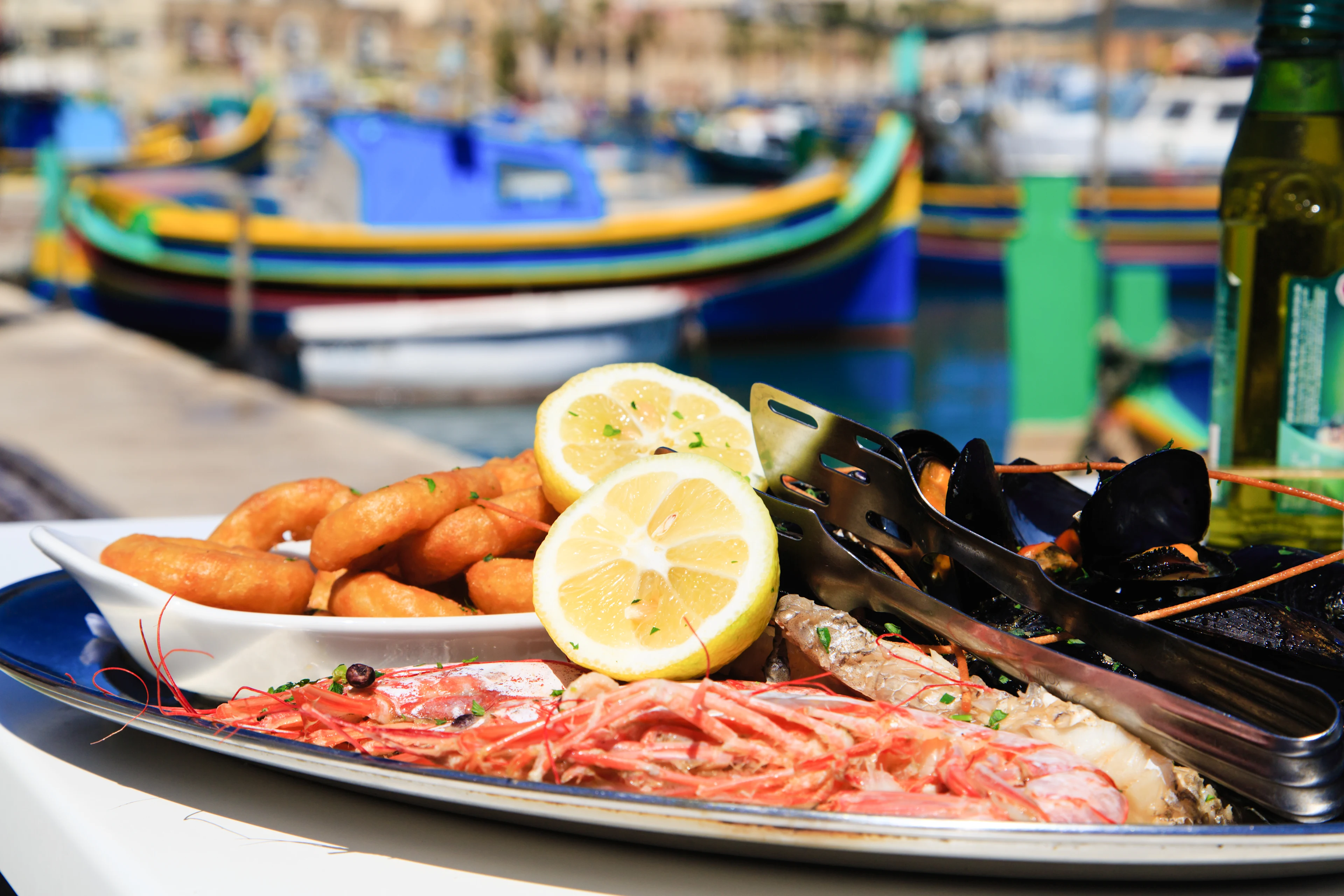 Fiske- og skaldyrsfad med rejer, muslinger og citron serveret i en havn på Malta.