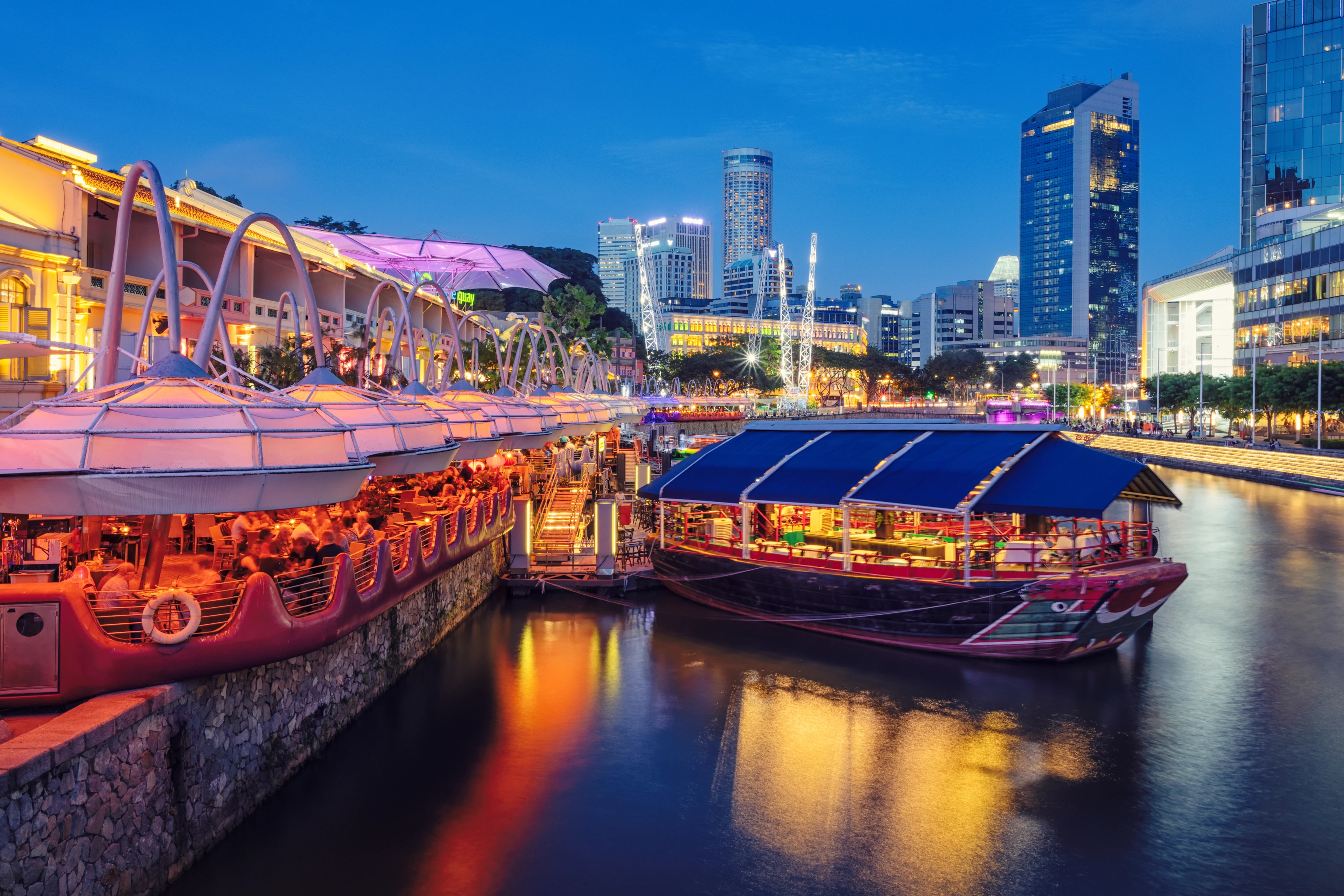 Upplysta restauranger och båtar längs Singapore River i Clarke Quay