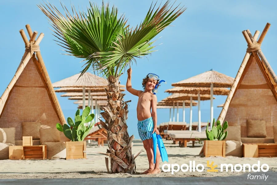 Jongen met cyclops op zijn hoofd en zwemvliezen in zijn hand naast een palmboom 