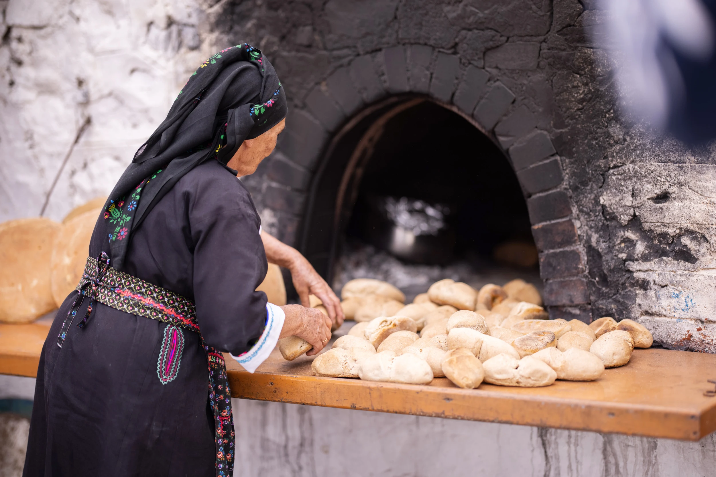 Kvinna i traditionell folkdräkt bakar bröd i vedeldad ugn i Olympos på Karpathos