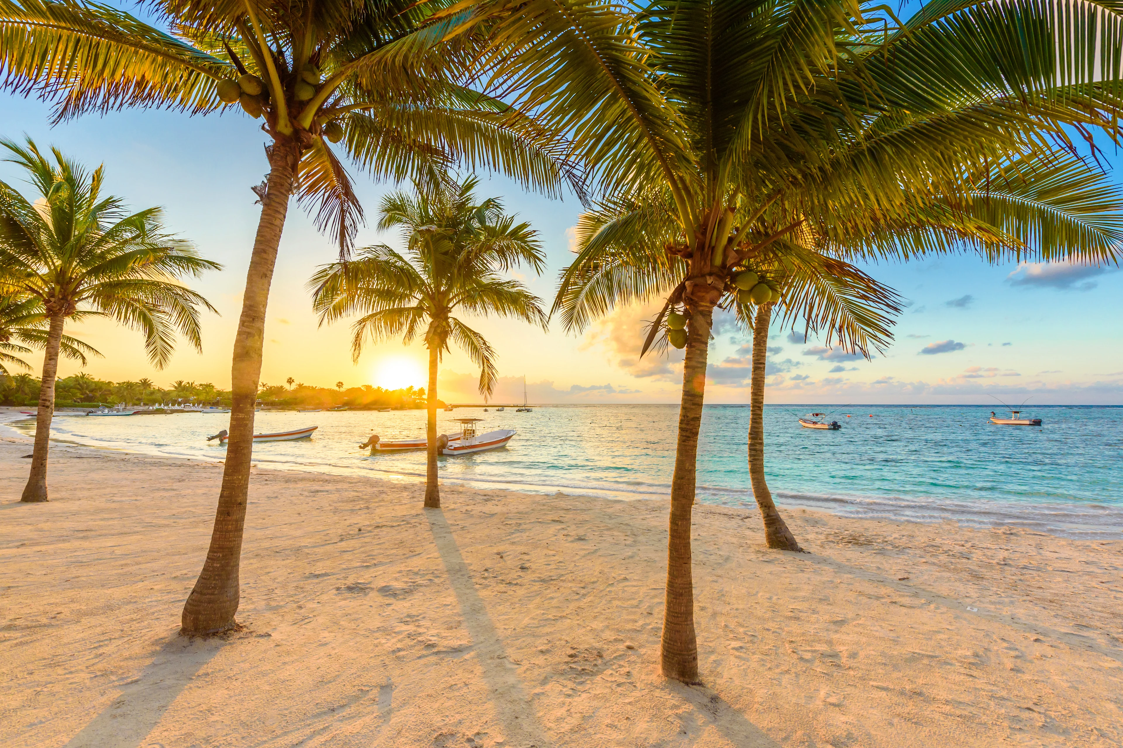 Vit sandstrand i Cancun, Mexico, med palmtakshytter, turkost hav och blå himmel – en perfekt plats för avkoppling.