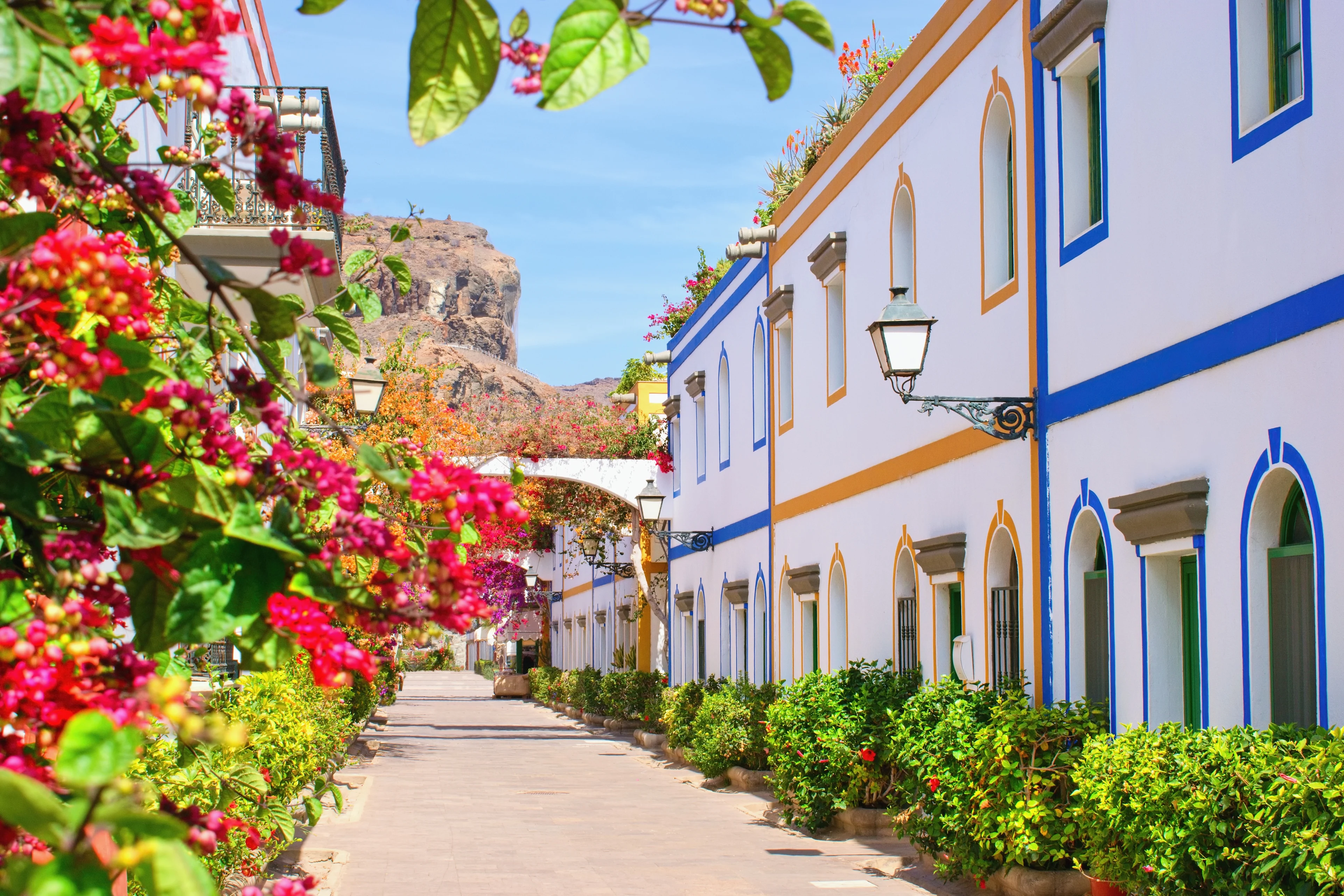 Färgglada hus med fönster och blommor i Puerto de Mogan under blå himmel.