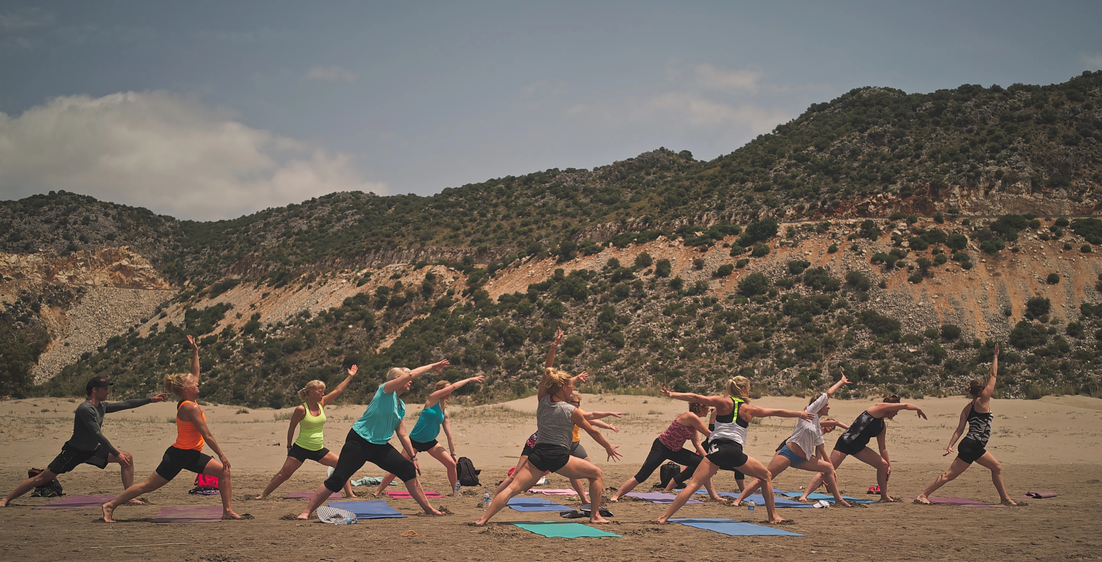 En grupp personer gör yoga på en strand med berg i bakgrunden