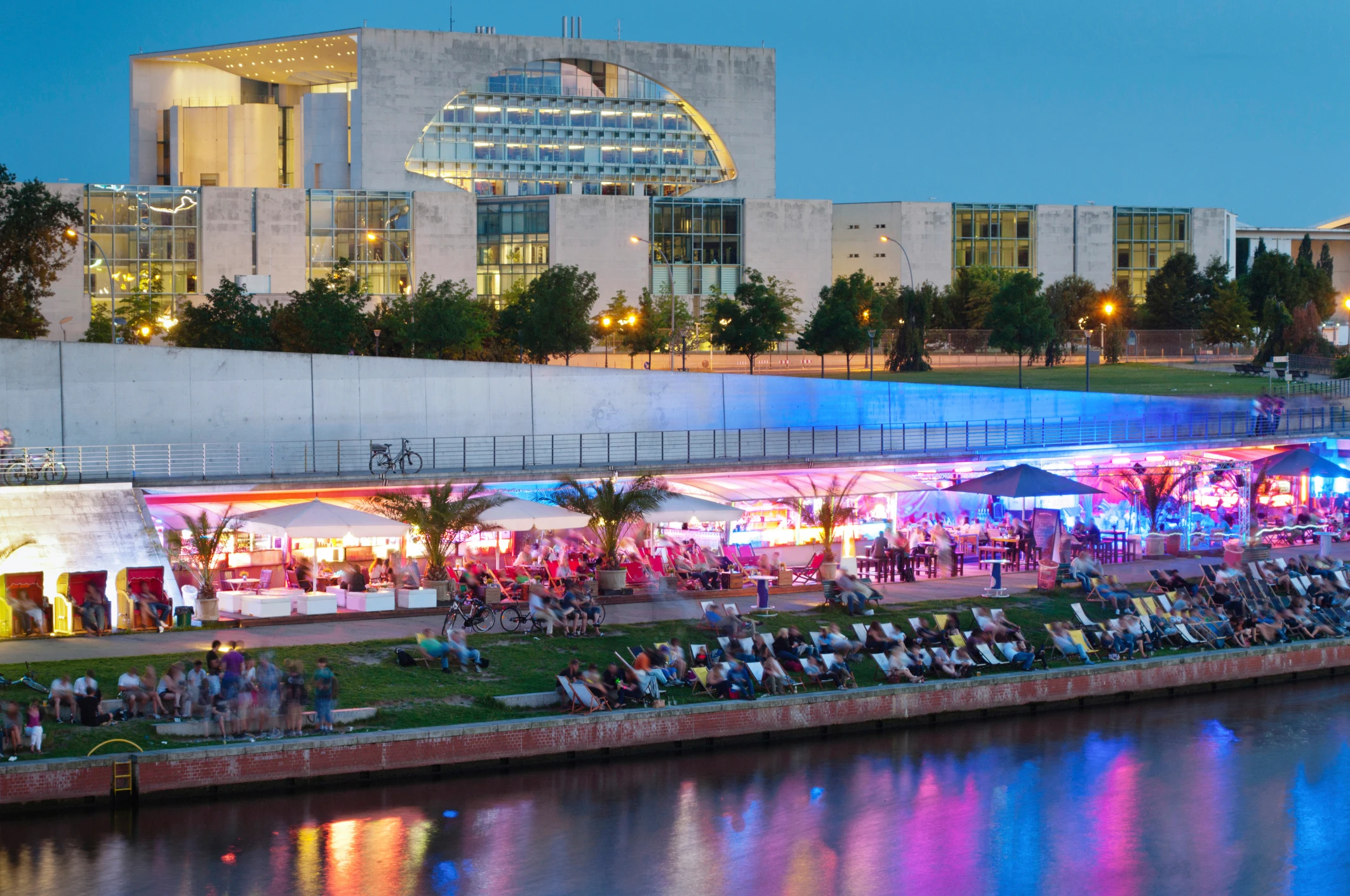 Kvällsvy över Berlin med floden Spree, en livlig strandbar och Bundeskanzleramt i bakgrunden.