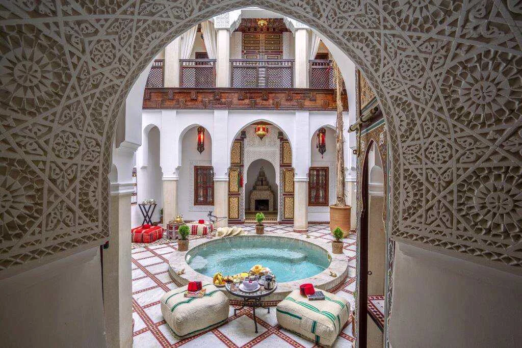 Traditionel gårdhave på Riad Safran et Cannelle & Spa i Marrakech med rund pool, marokkanske siddepladser, hvide buer og dekorative detaljer i træ og sten.