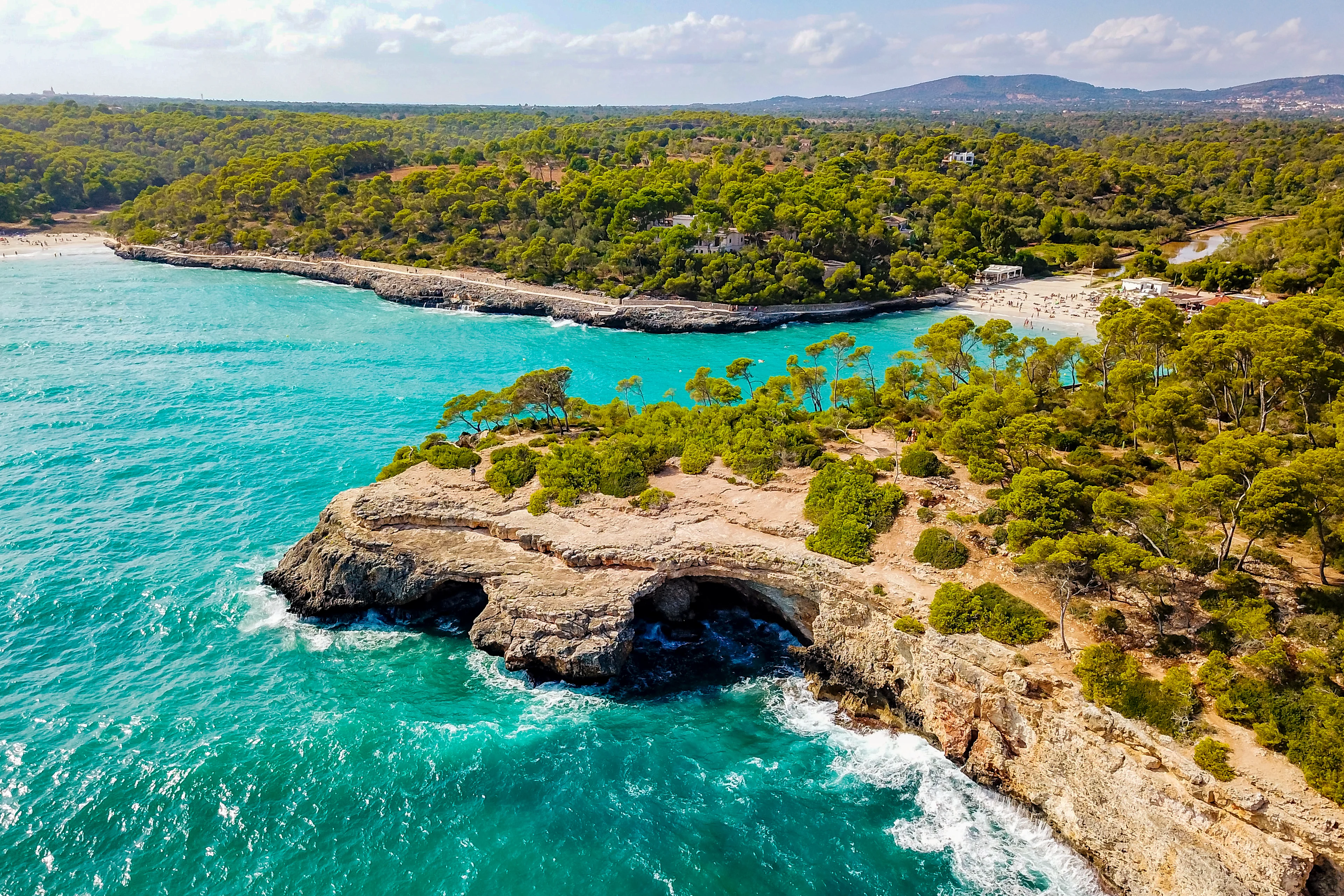 Flygfoto över kusten med klippor, turkost vatten och gröna träd på Mallorca
