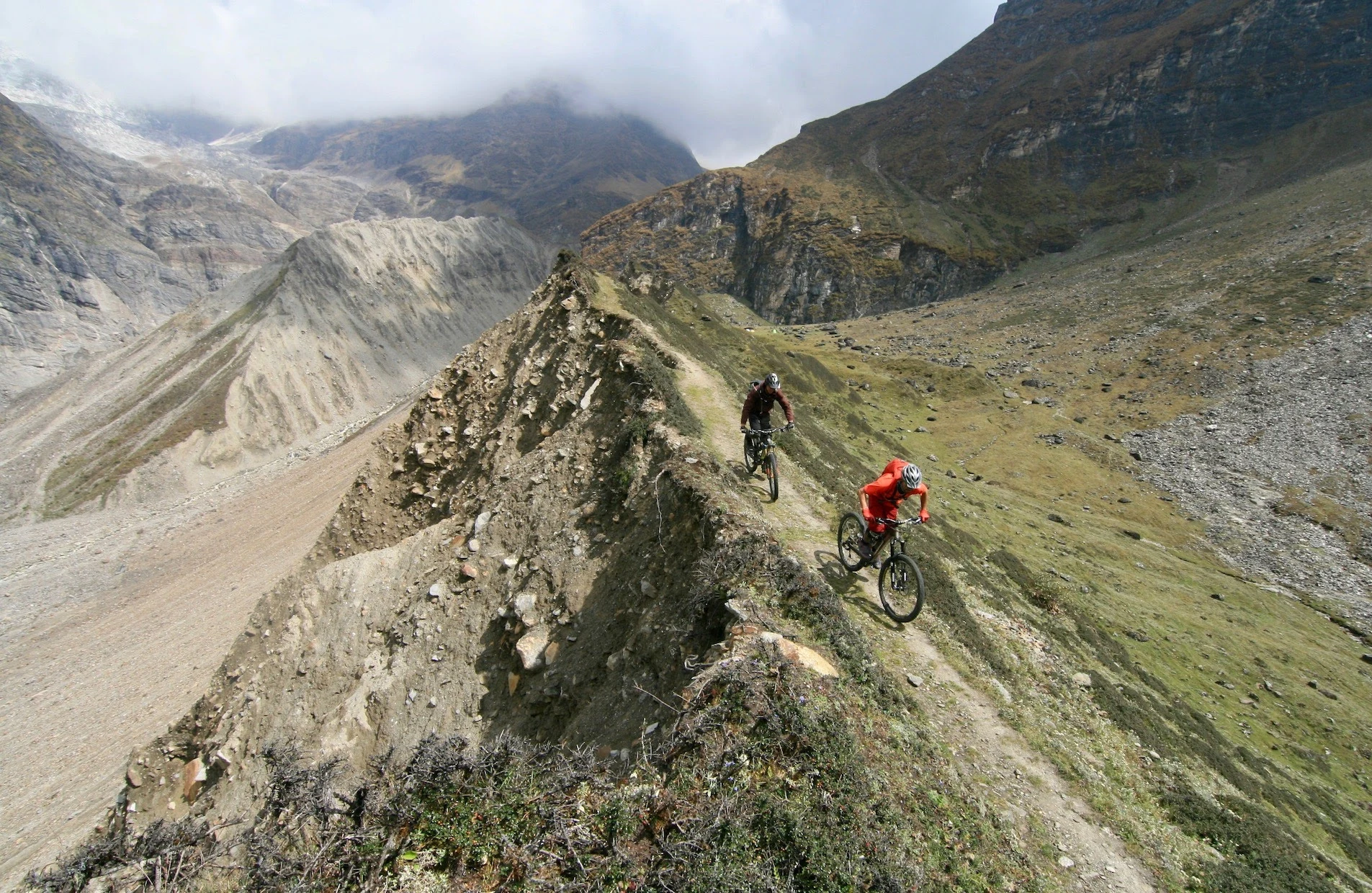 Två mountainbikecyklister färdas längs en smal bergsrygg i ett dramatiskt, högalpint landskap