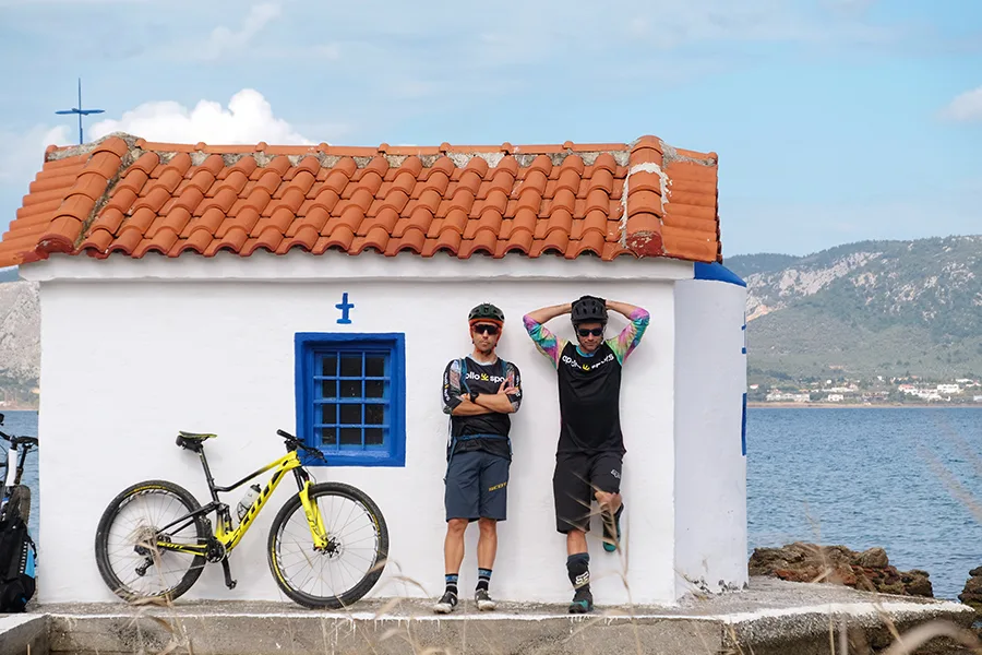 Två män står lutade mot en husvägg bredvid en cykel