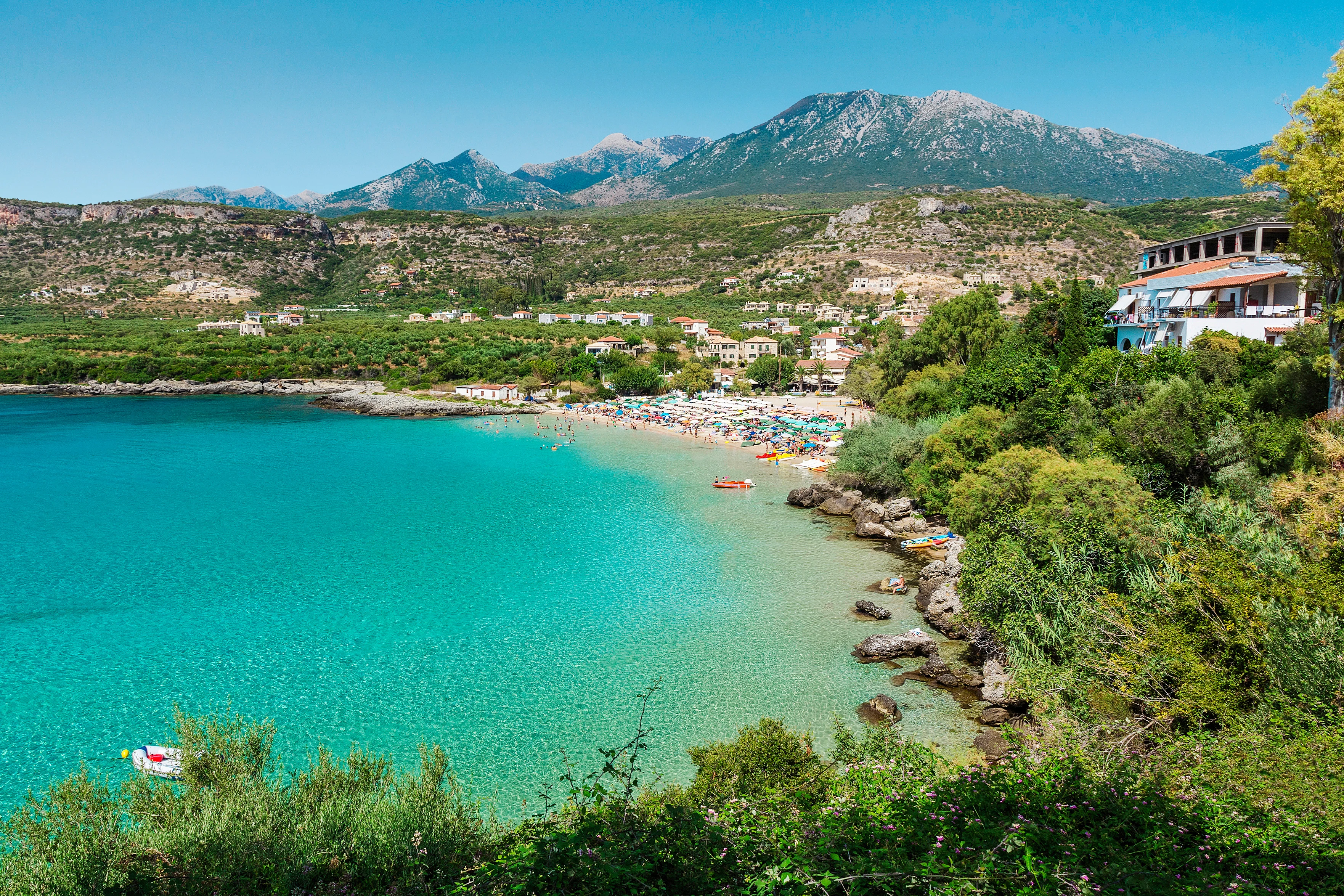 Turkis badebukt i Stoupa i Hellas med sandstrand, grønn natur og fjell i bakgrunnen.