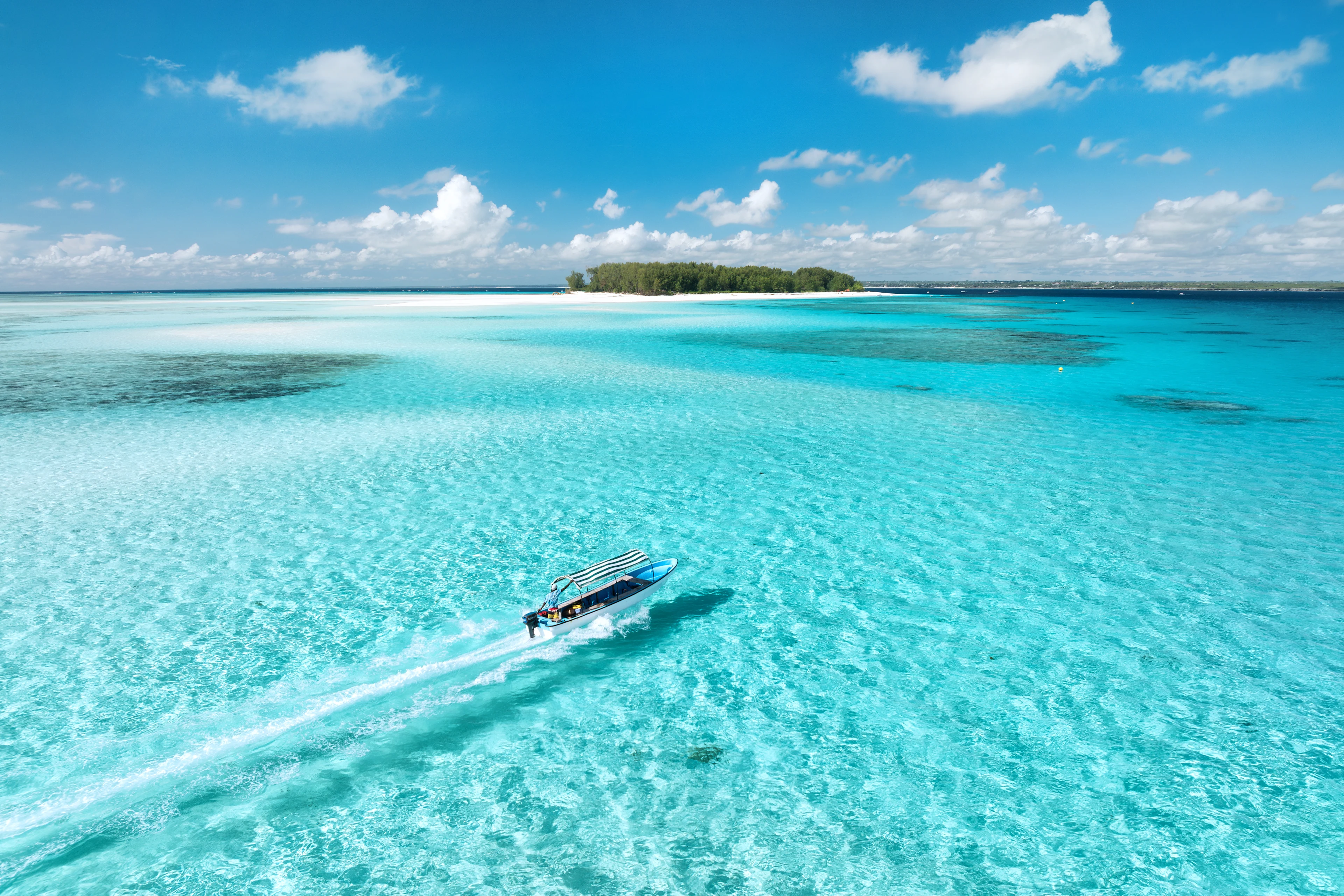 En vacker strand på Zanzibar med vita sandstränder och turkost vatten. Höga palmer sträcker sig mot den klarblå himlen. Flera små hyddor med halmtak finns utspridda på stranden.