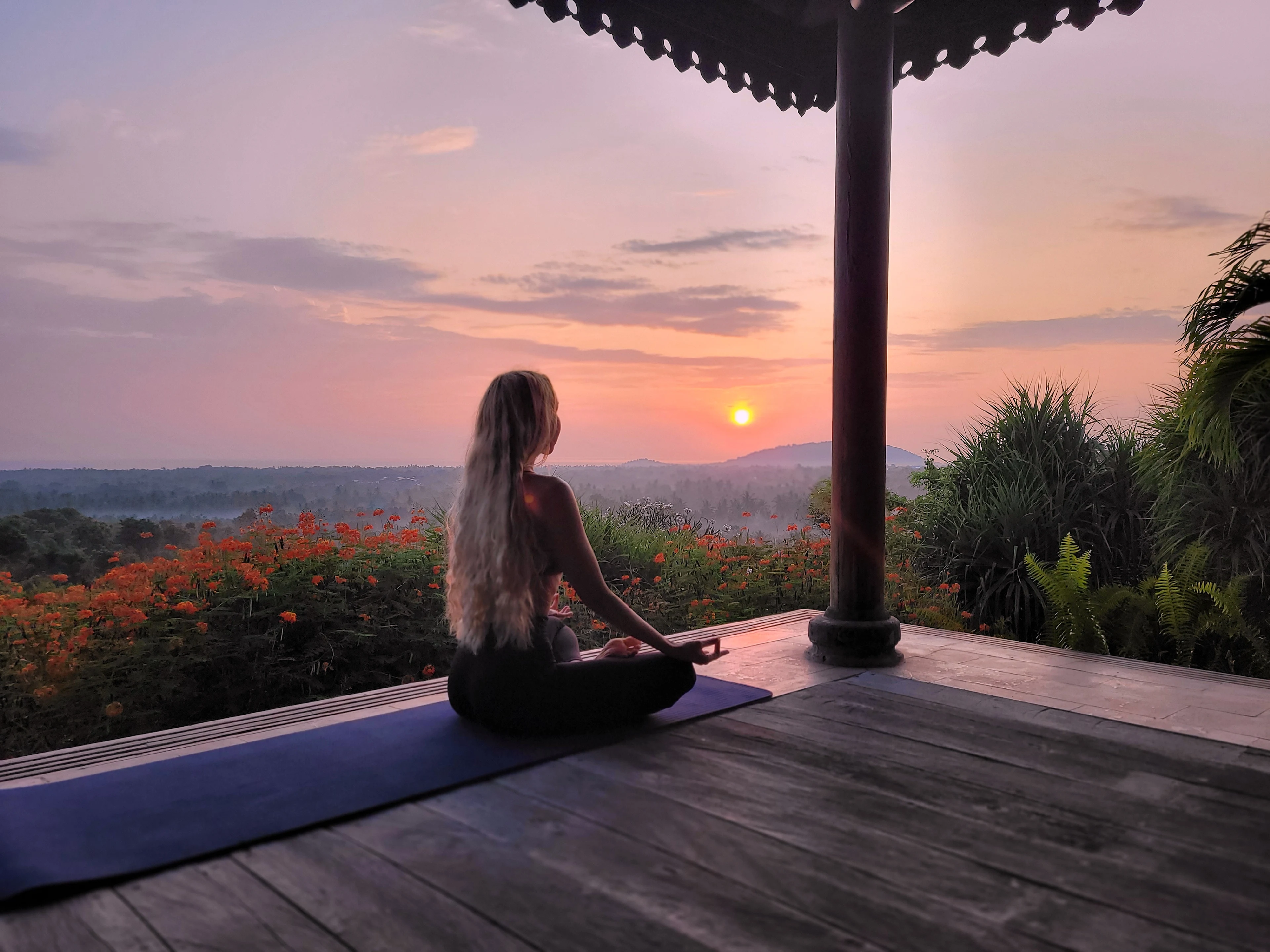 Kvinde praktiserer yoga med skov og solnedgang i baggrunden
