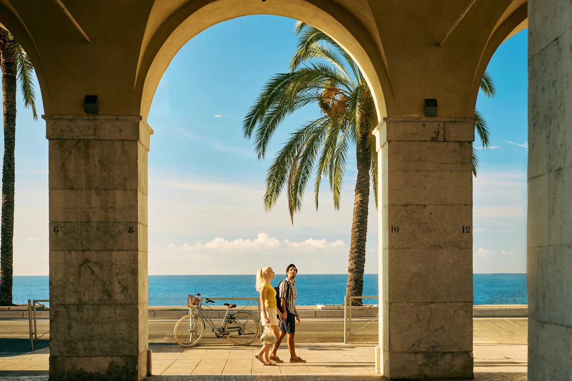Palmetræ og promenade i Nice ved Middelhavet, indrammet af en stenarkade.