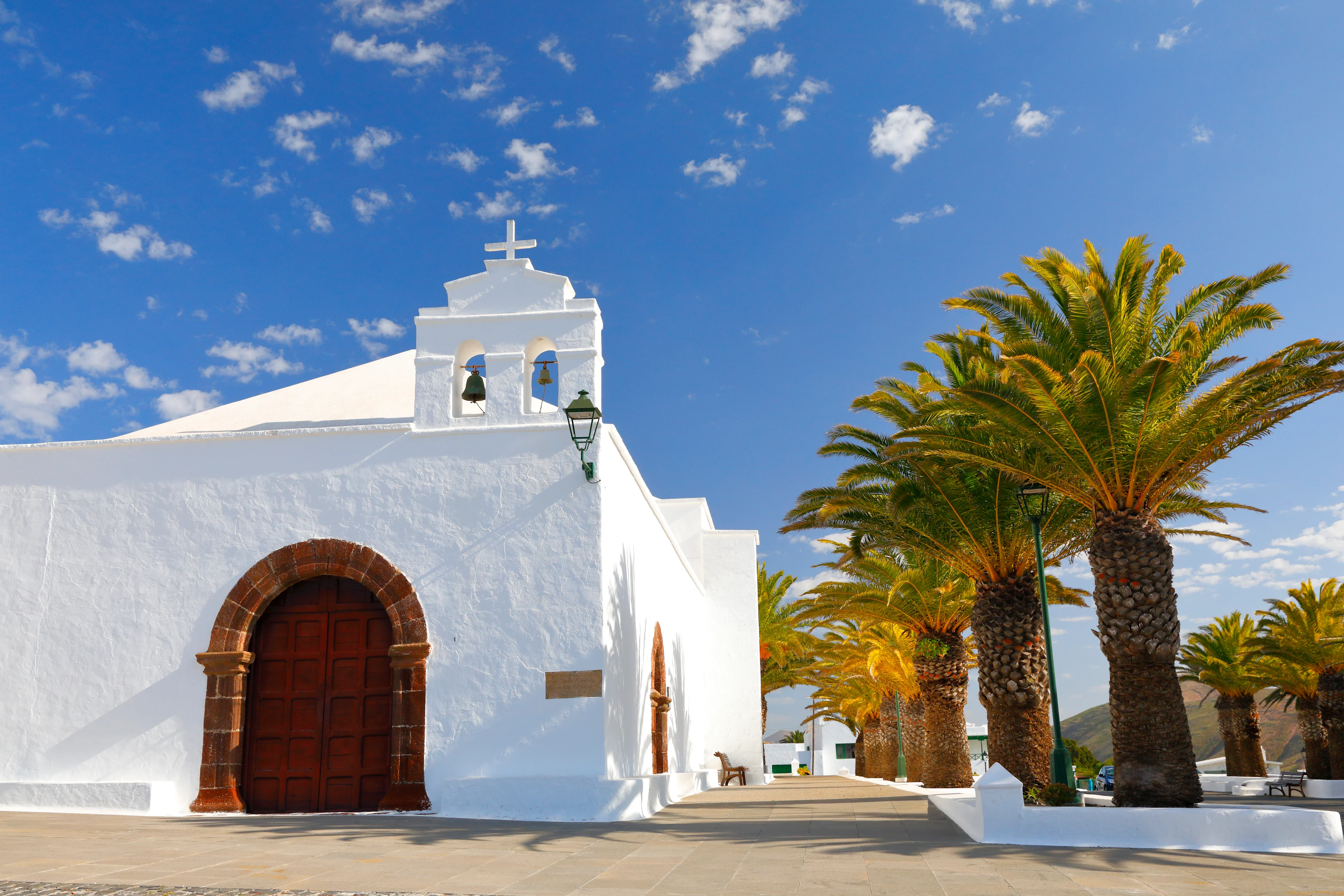 Vitkalkad kyrka i byn Femés på Lanzarote, omgiven av palmträd och med utsikt över öns vulkaniska landskap.