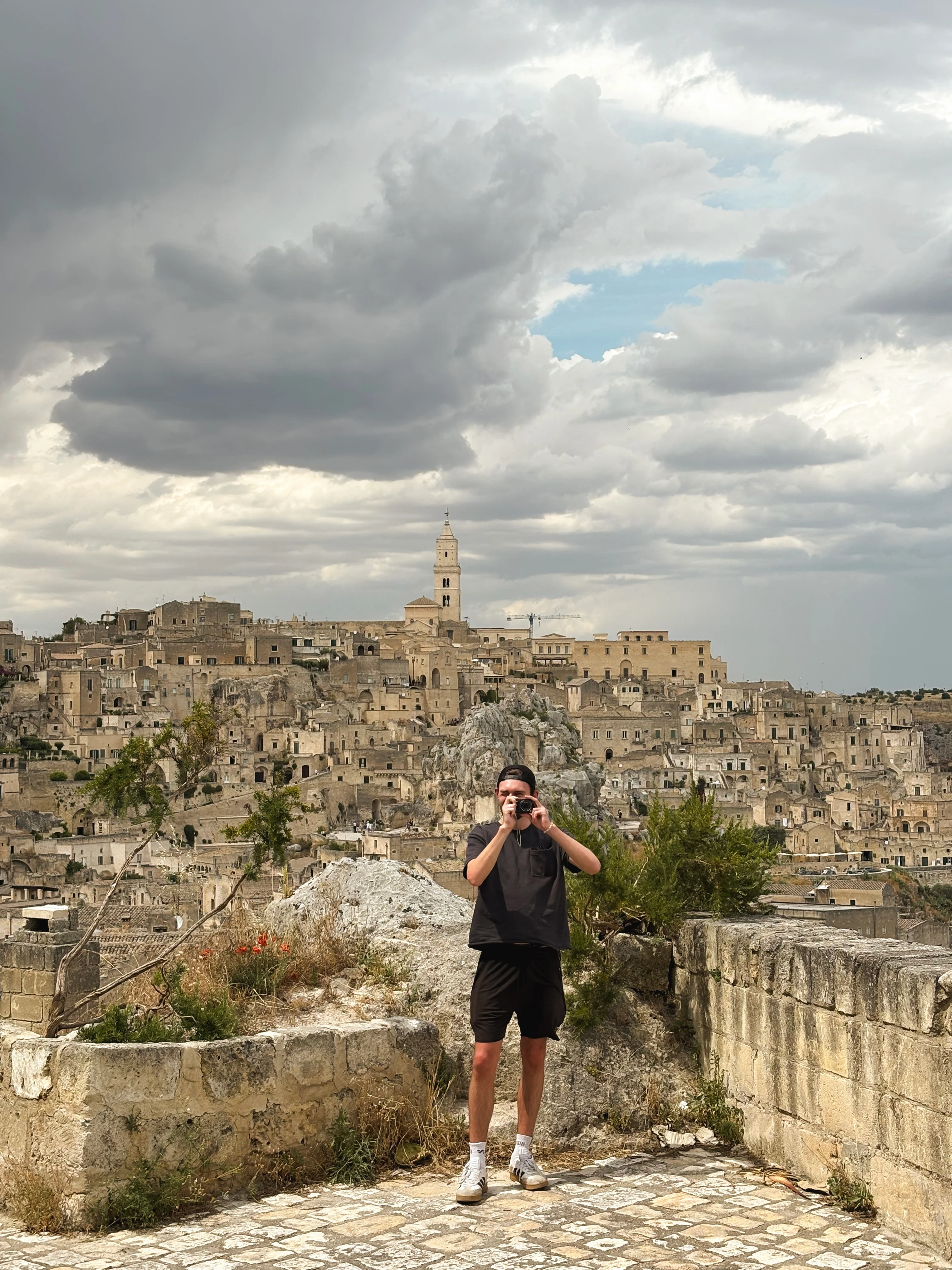 Person på utsiktsplats med vy över historiska Matera under dramatisk himmel.