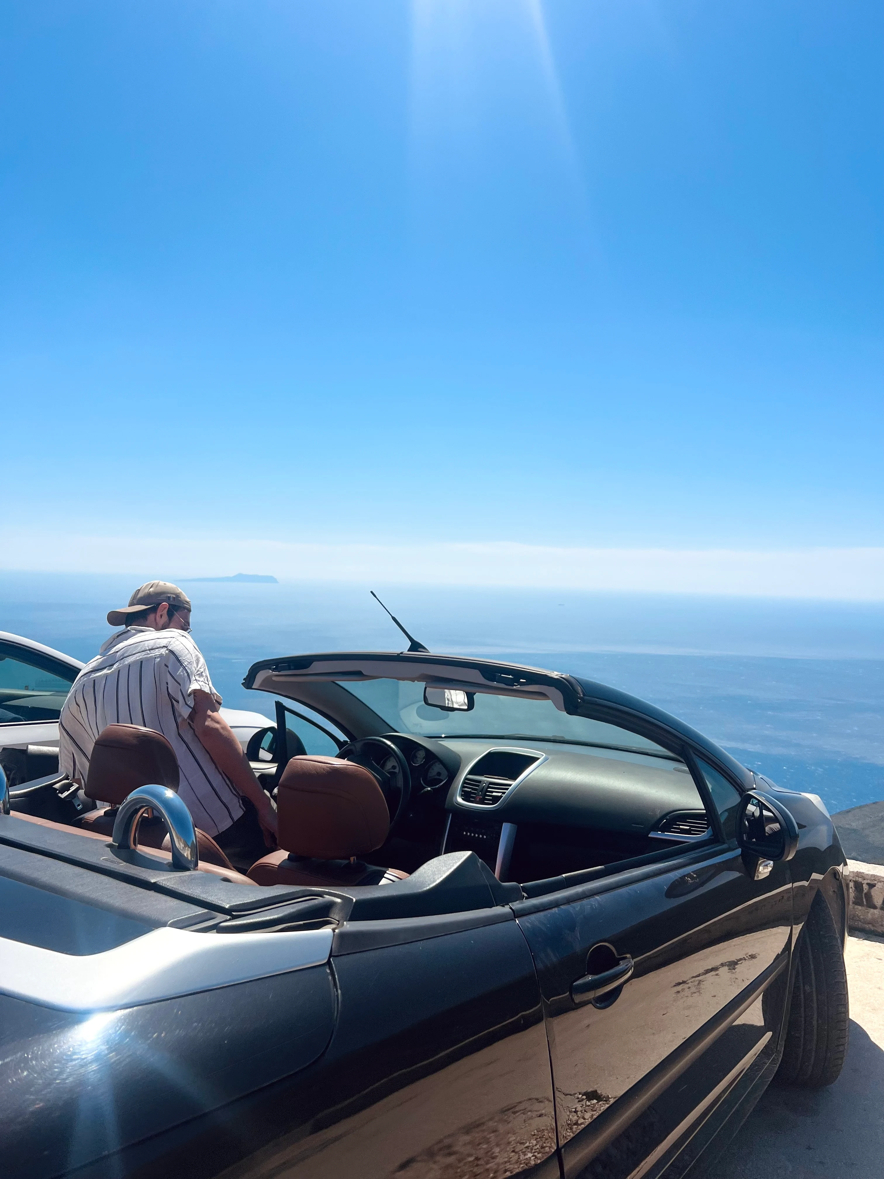 En person som kliver in i en bil med havet och blå himmel i bakgrunden. 