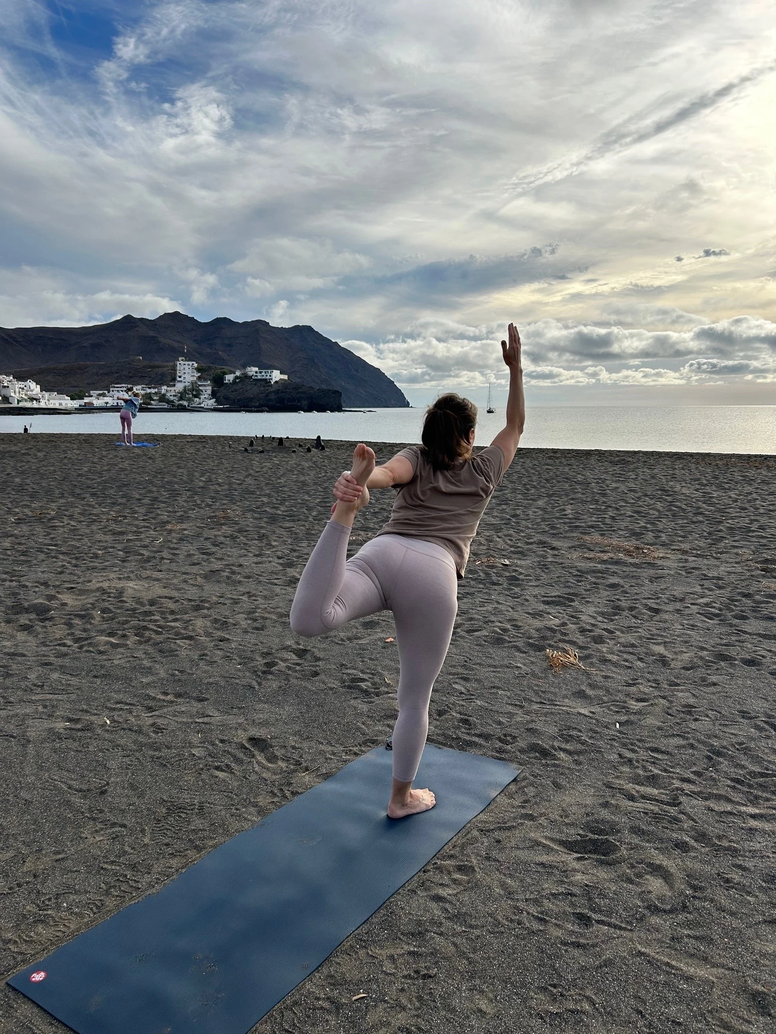 Dame som står i yogaposisjon på en yogamatte på stranden