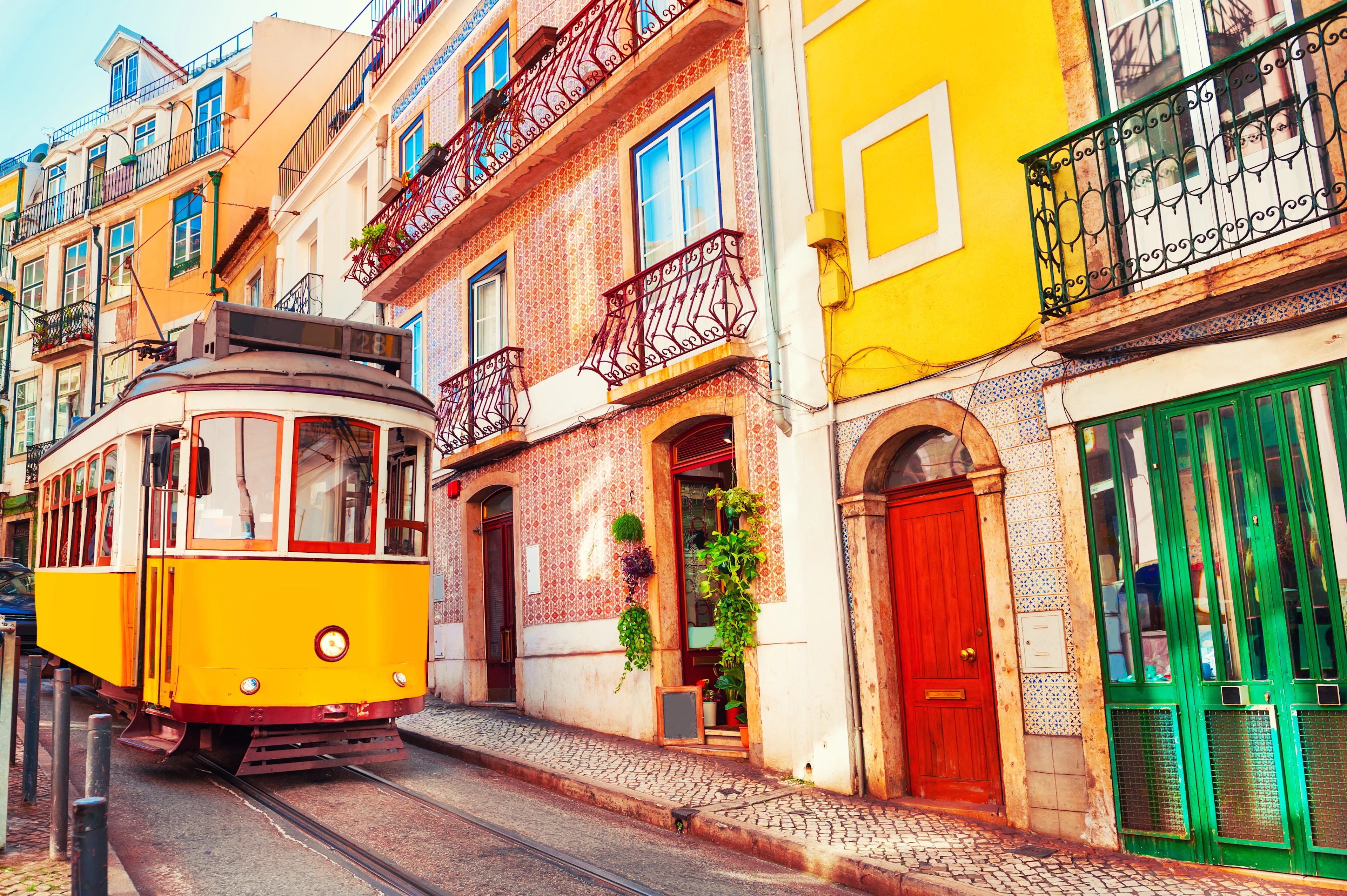 Klassisk gul spårvagn på en smal gata kantad av färgglada hus och kakelprydda fasader i Lissabon, Portugal.