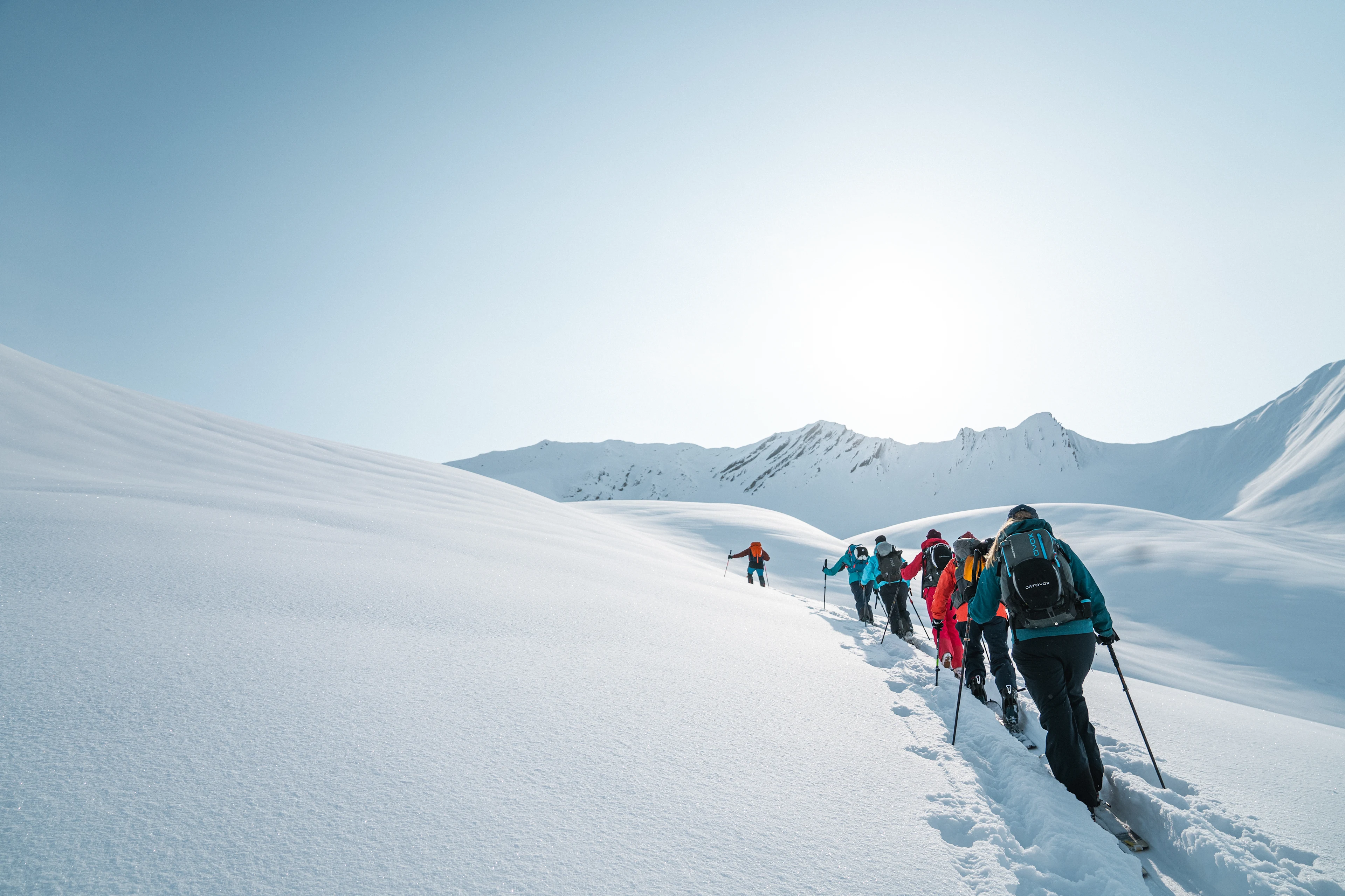Grupp på topptur vandrar genom snötäckt fjällandskap med skidor och stavar.