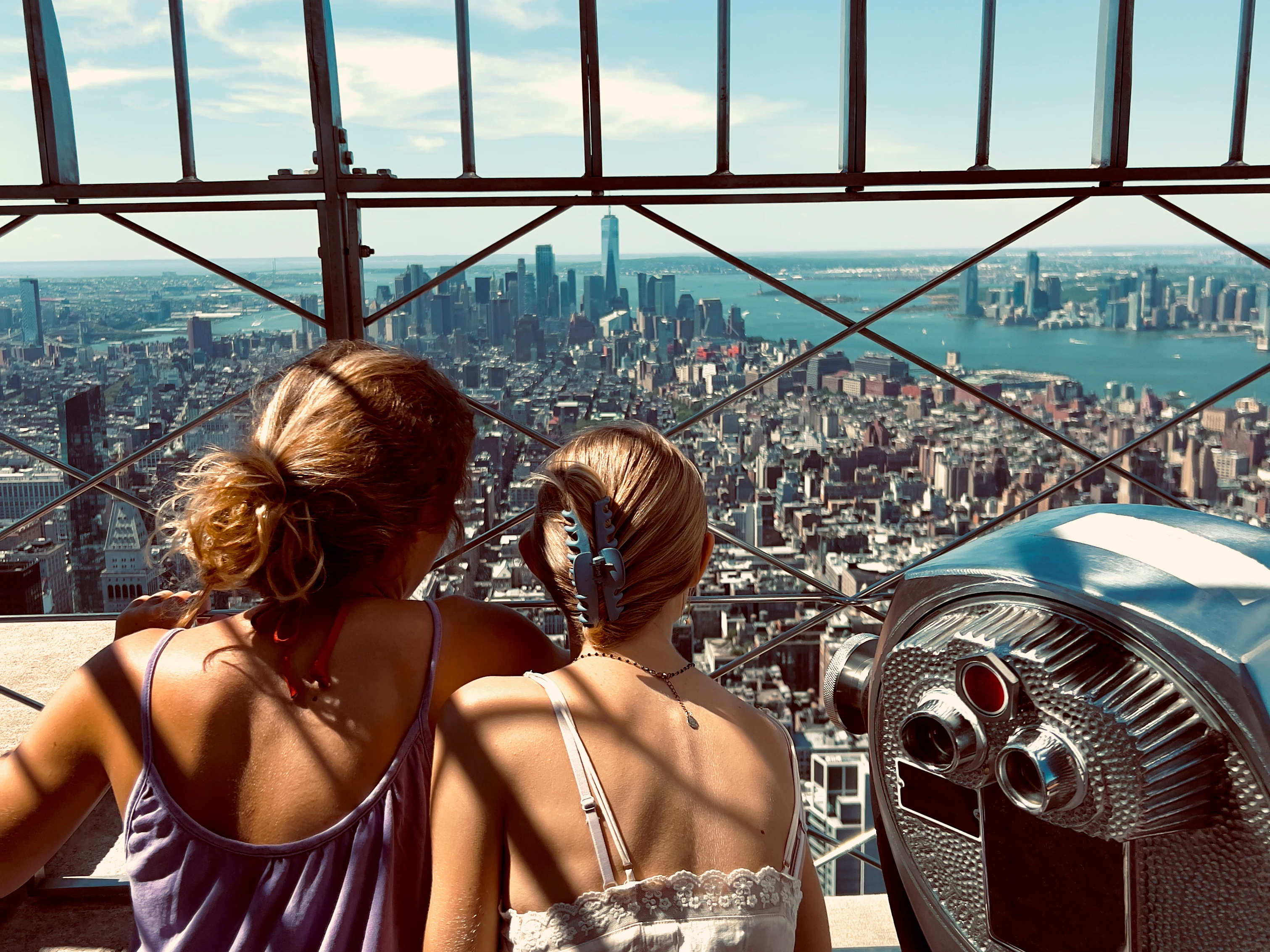 Två tonårstjejer blickar ut över Manhattan från Empire State Buildings observationsdäck med One World Trade Center i bakgrunden.