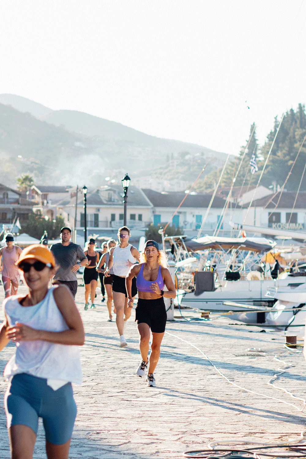 personer som springer på en hamnpromenad med berg i bakgrunden 
