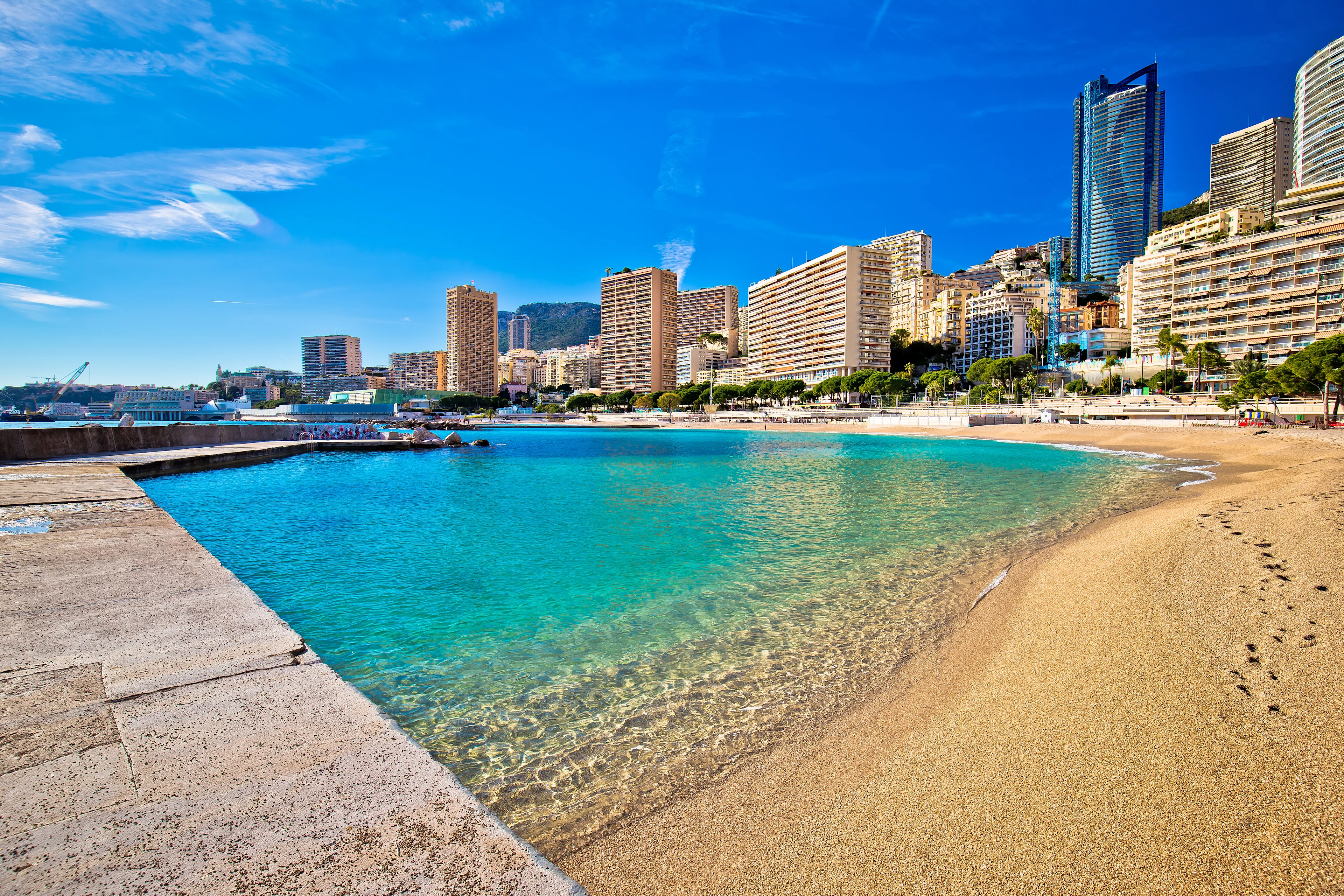 Larvotto Beach i Monaco med turkost vatten, ljus sandstrand och utsikt över stadens välkända skyline längs Medelhavskusten.