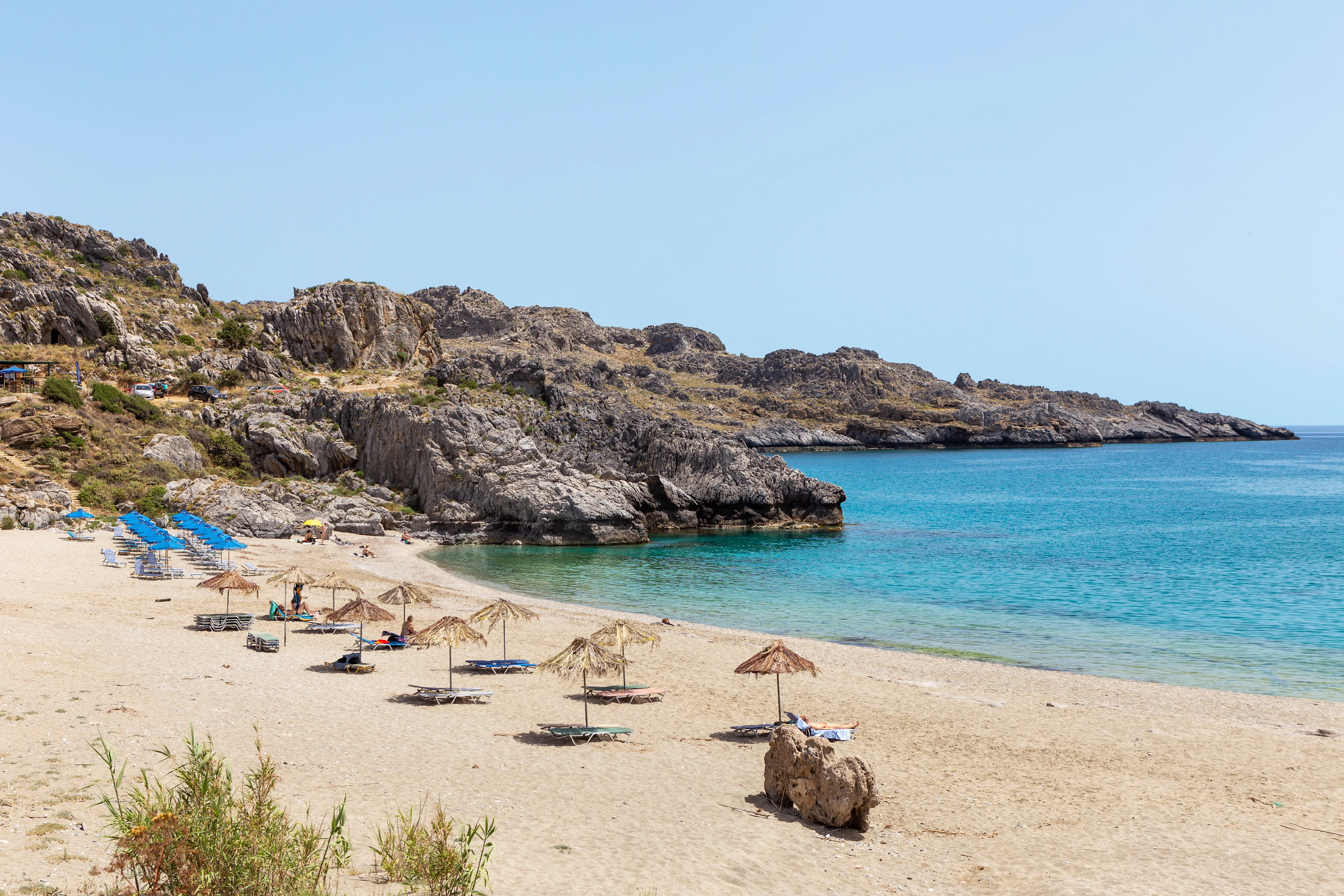 Ligstoelen en parasols op een zandstrand met kristalhelder water in Plakias op Kreta
