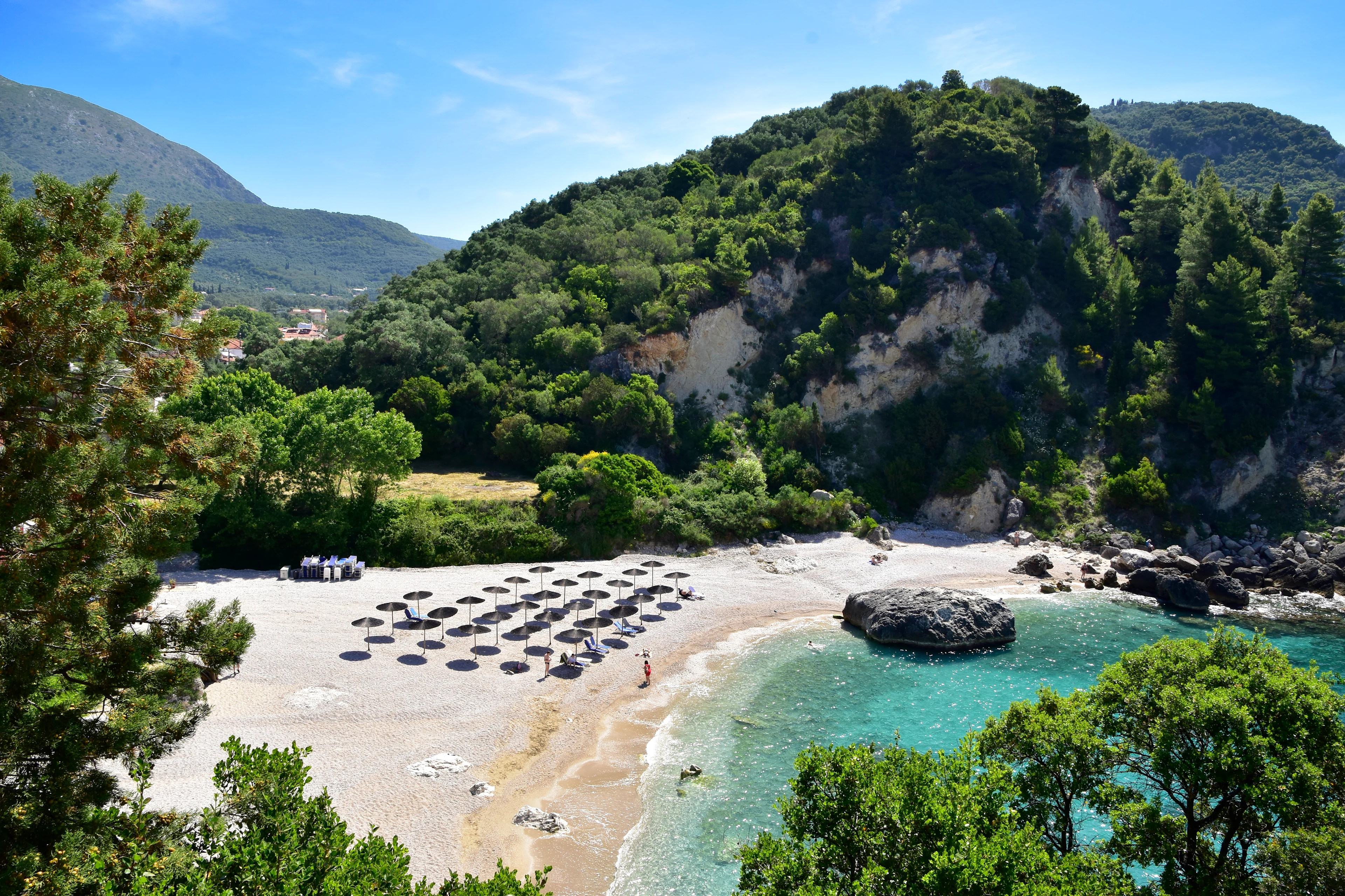 Hvit sandstrand med parasoll og solsenger mellom grønnkledde åser