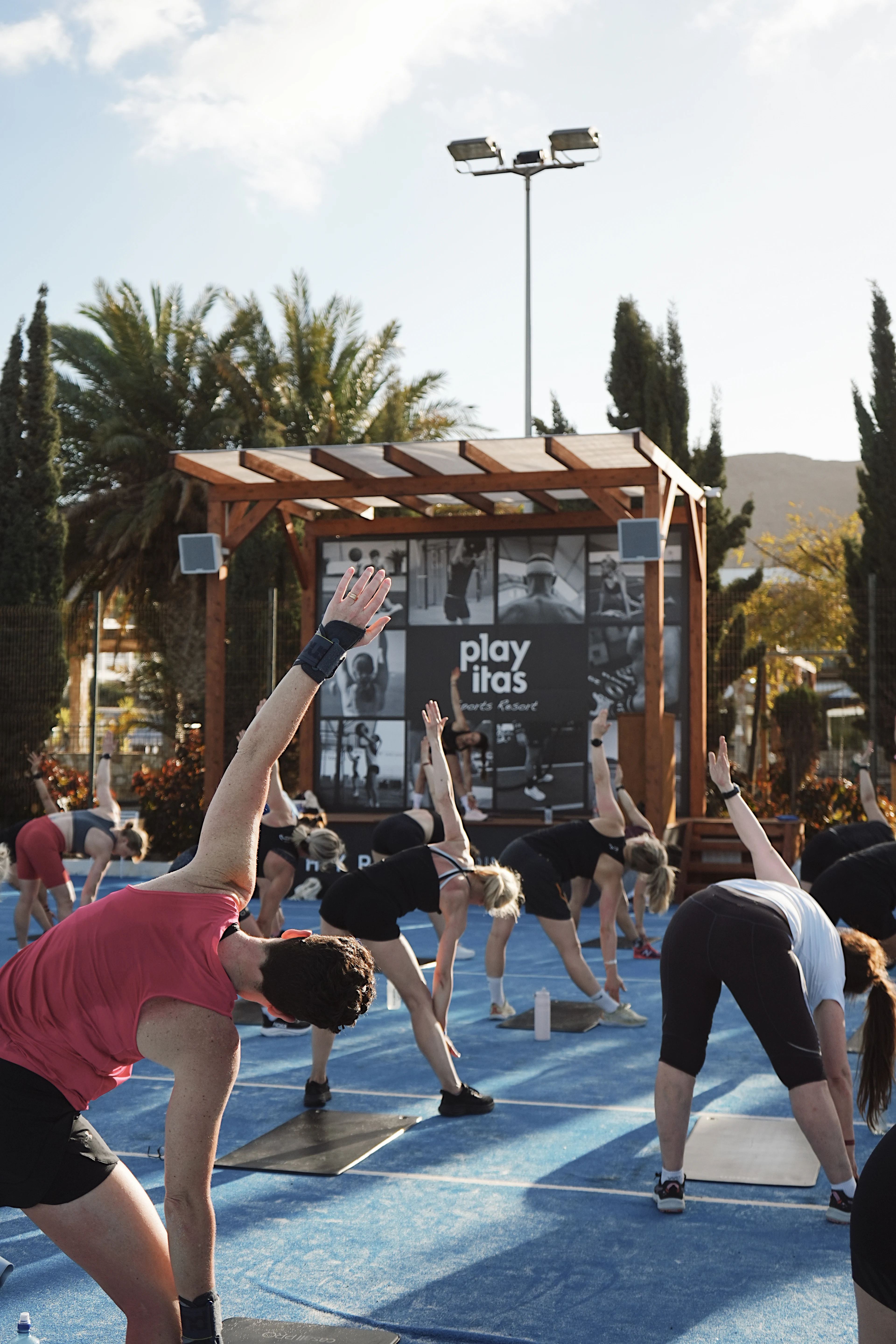 Gruppe med folk som trener og tøyer på et område foran en treningsplattform utendørs
