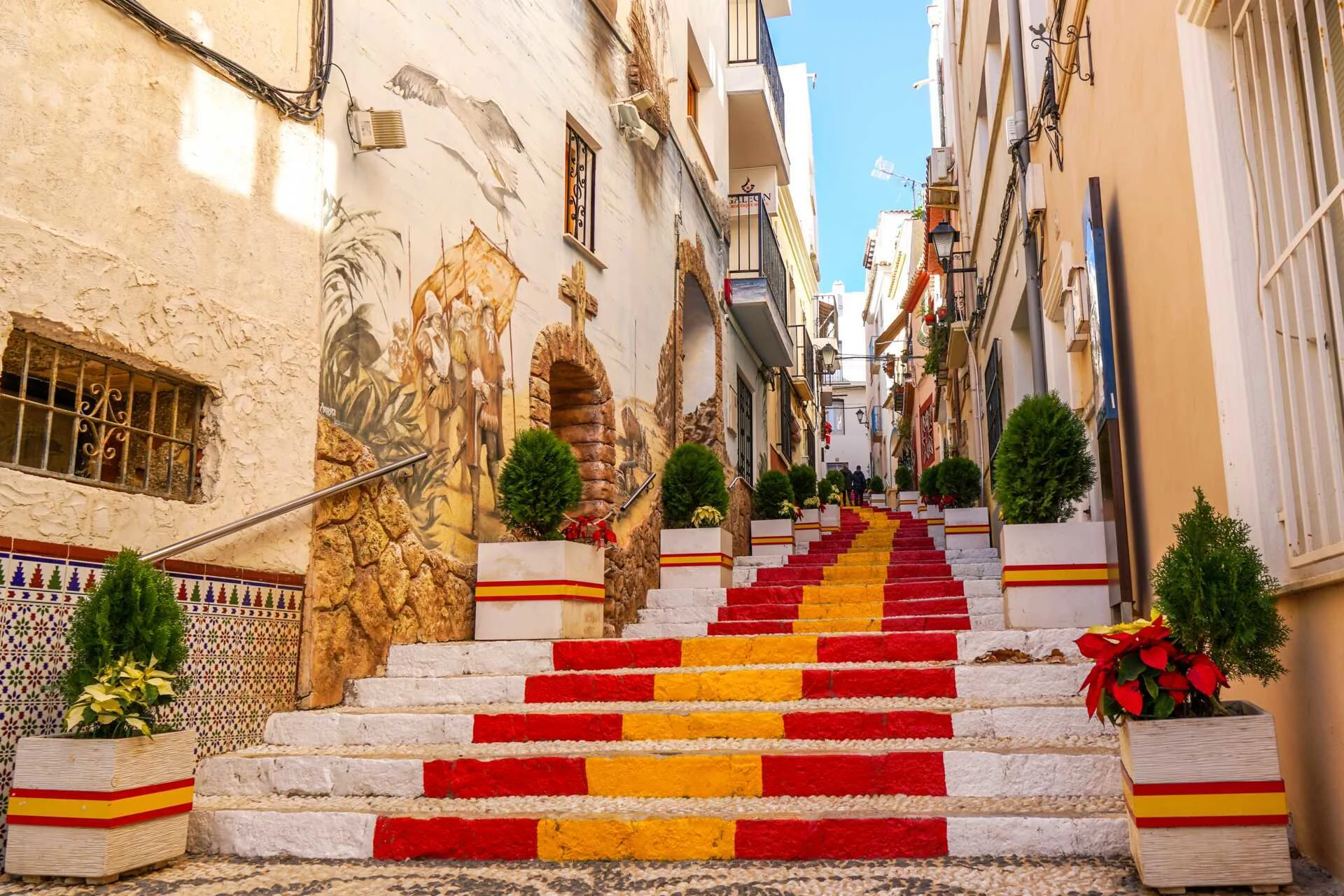 Trappa målad i rött och gult i en smal gränd, med murverk, väggmålningar och krukväxter; färgerna motsvarar den spanska flaggan.