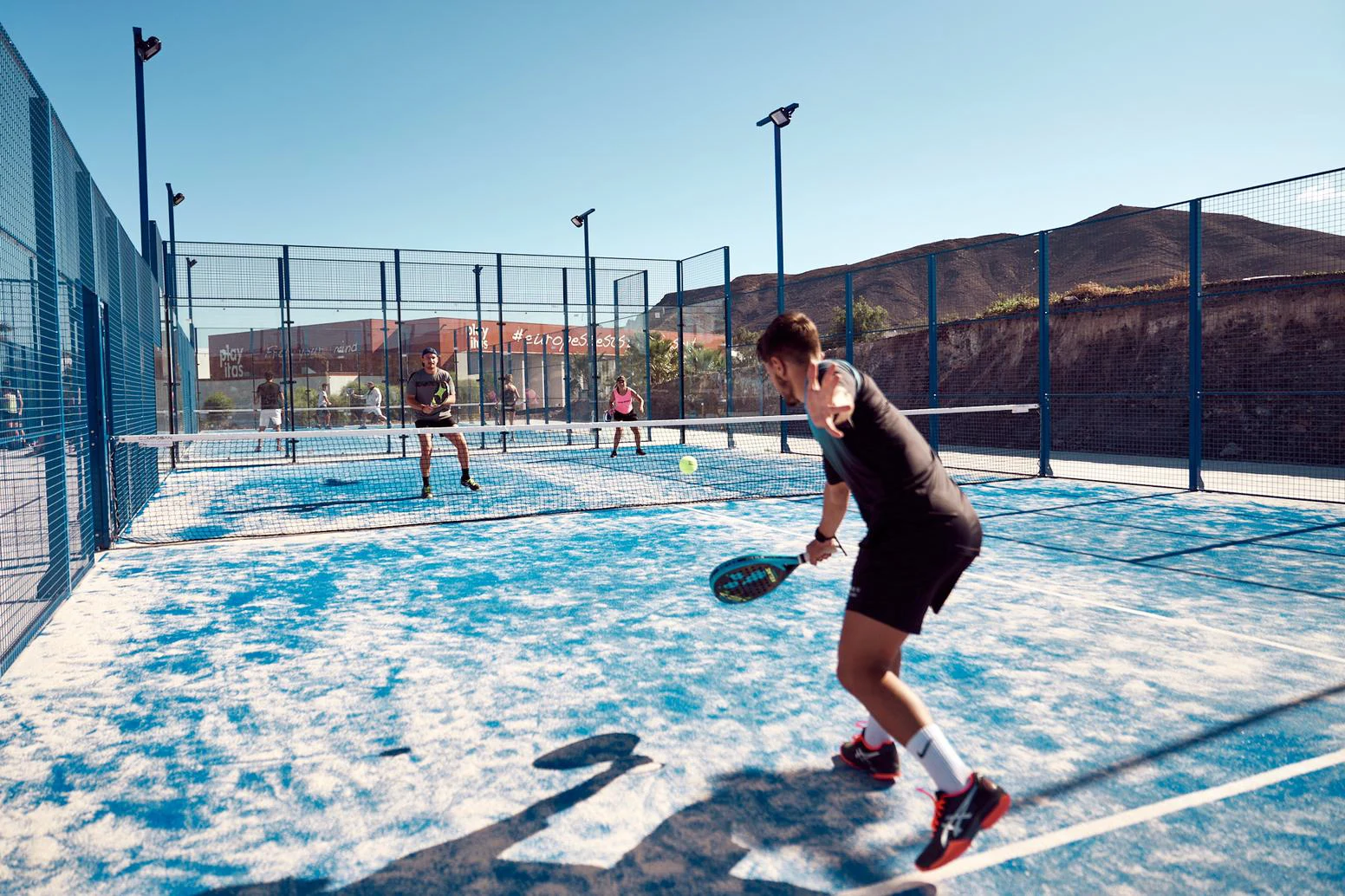 tre personer som spiller padel ute i solen