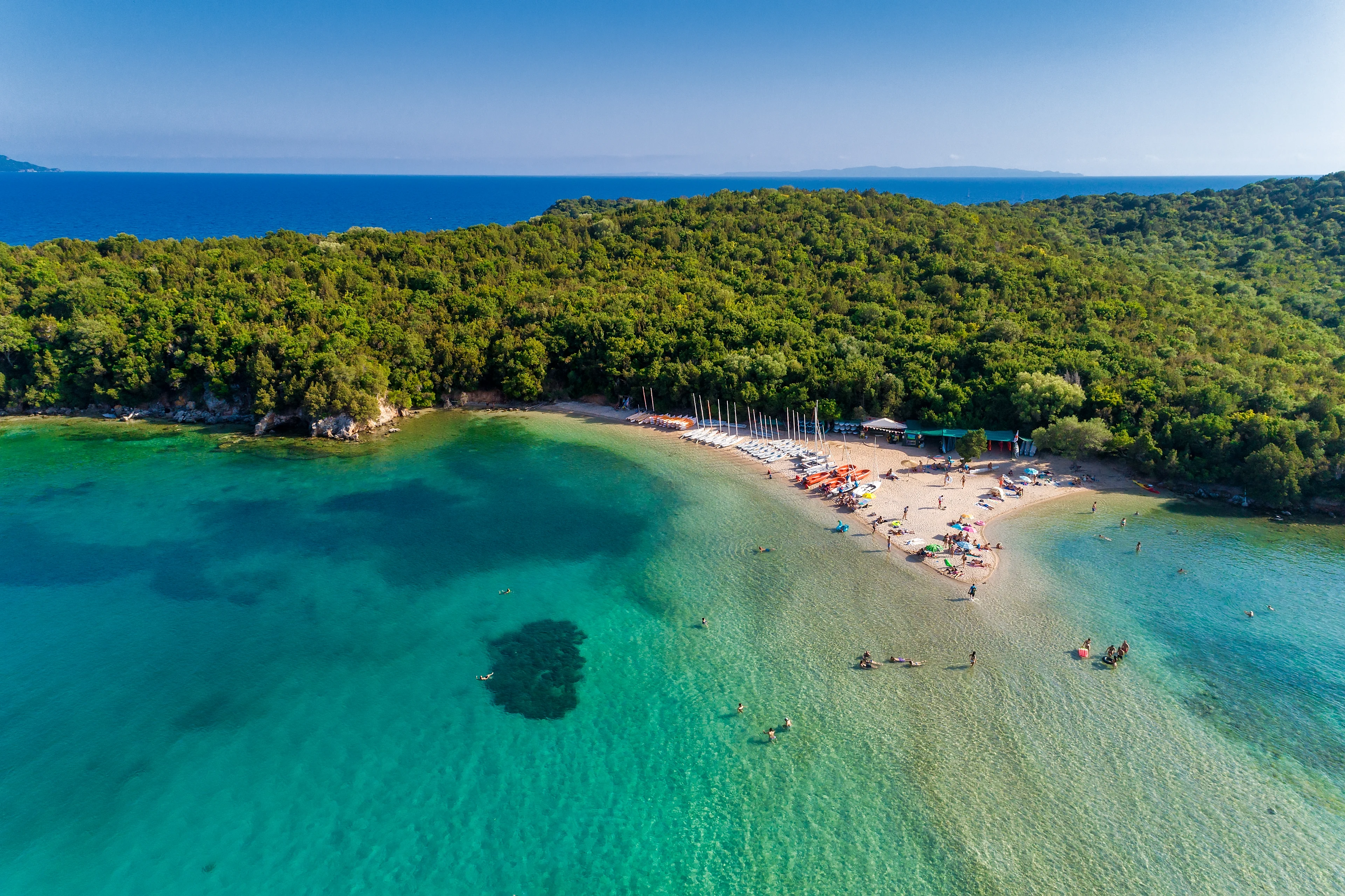 Turkos badvik med sandstrand och kristallklart vatten i Sivota, omgiven av grönskande natur