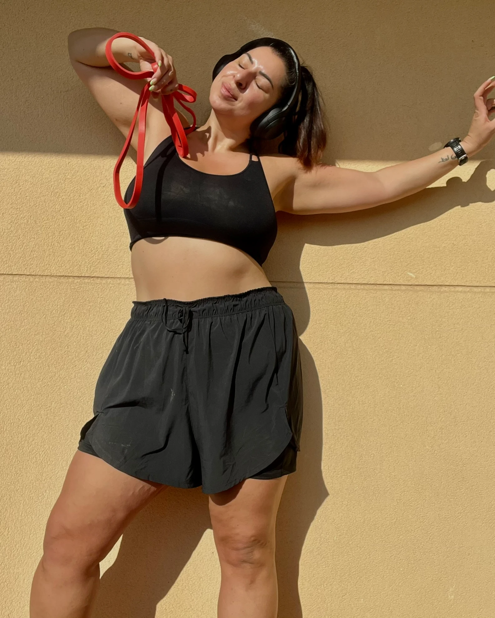 Bilde av Nastaran i sort treningstopp og shorts med en rød strikke i hånden som står mot en lys gul vegg