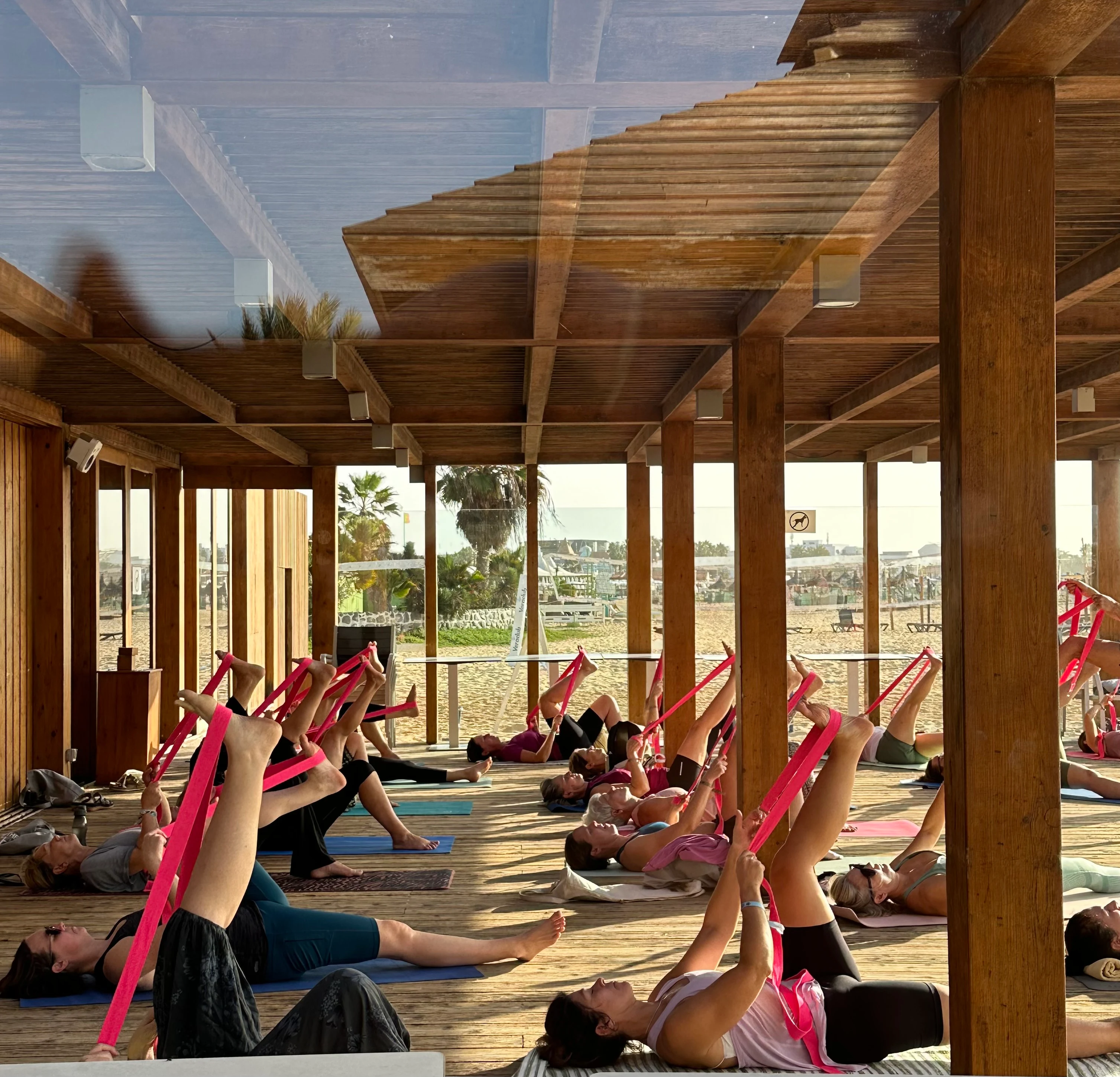 Grupp som deltar i ett yogapass med träningsband i en öppen paviljong vid stranden