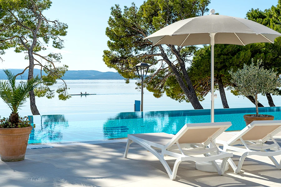 Infinitypool vid hotell vid Medelhavet i Kroatien med solstolar, parasoll, pinjeträd och utsikt över havet.