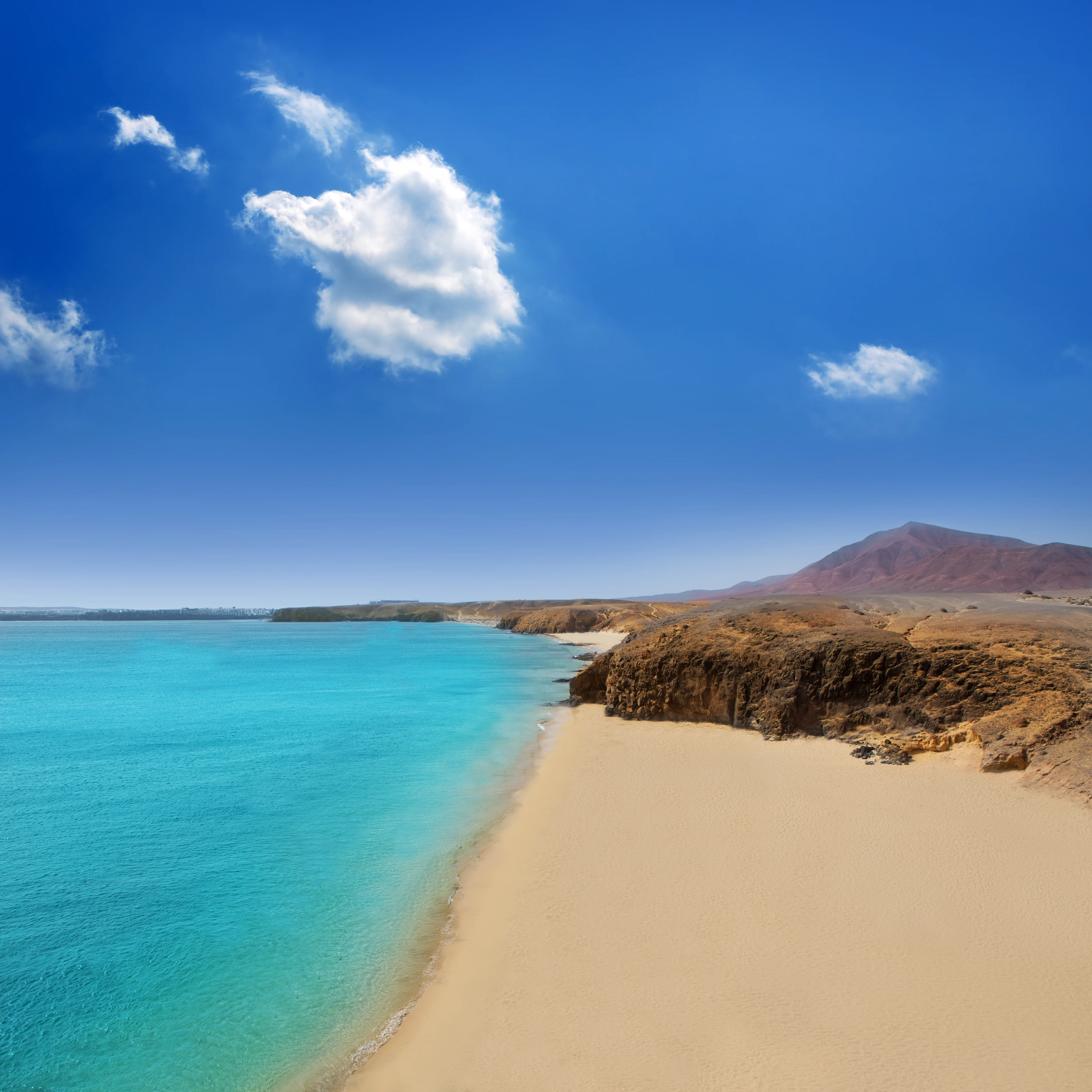 Playa del Pozo, jossa on vaalea hiekkaranta, turkoosi meri ja tulivuorimaisia maisemia kirkkaan sinisen taivaan alla.