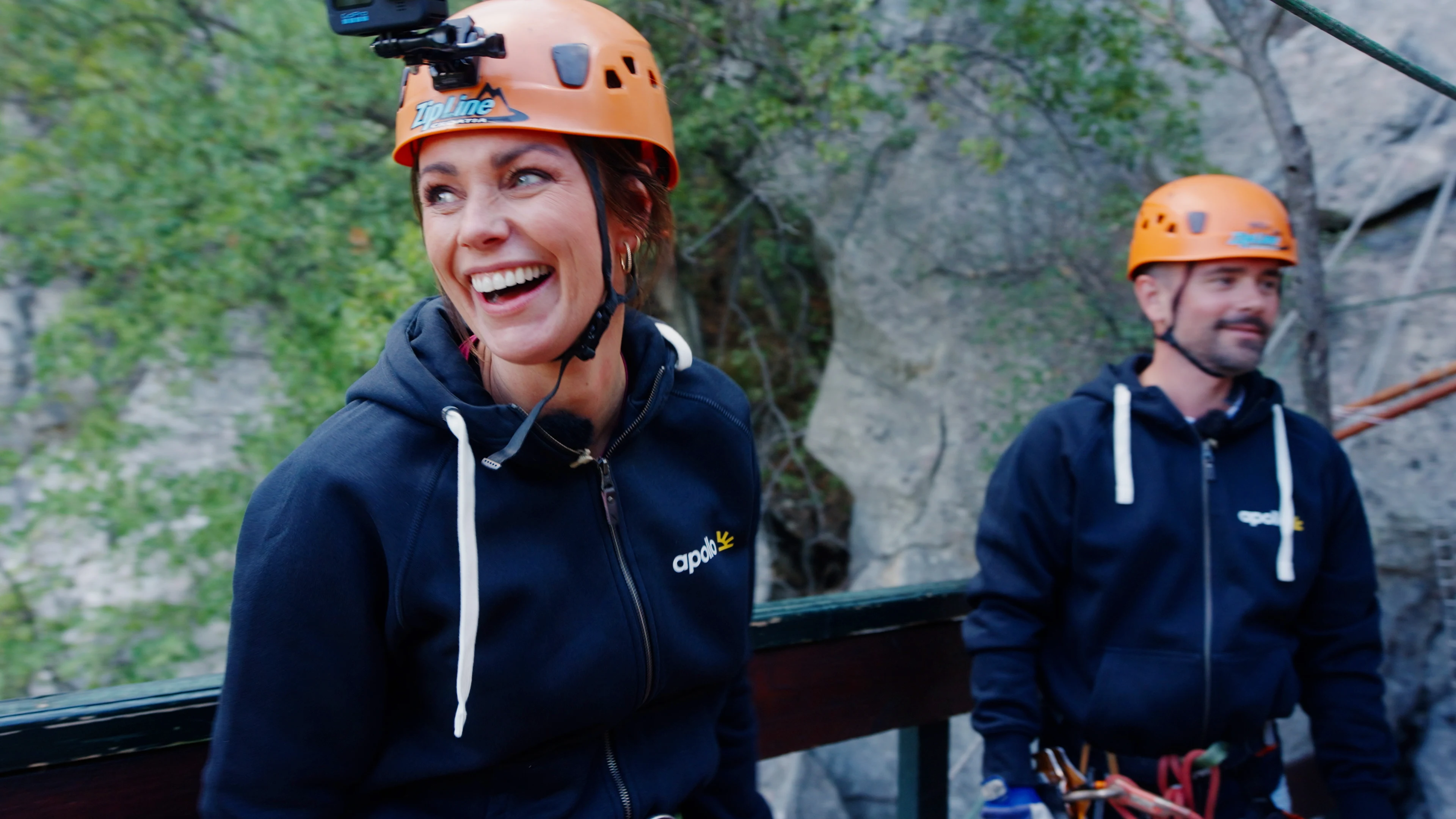 Två personer uppe i bergen med hjälm och redo för att åka zipline