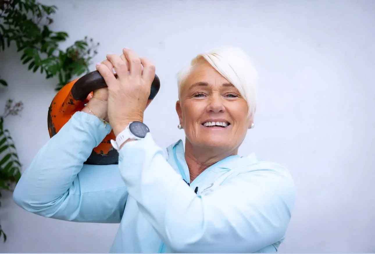 Siv Gunnarsen kledd i lys blå treningsjakke med en oransje kettlebell i hendene.